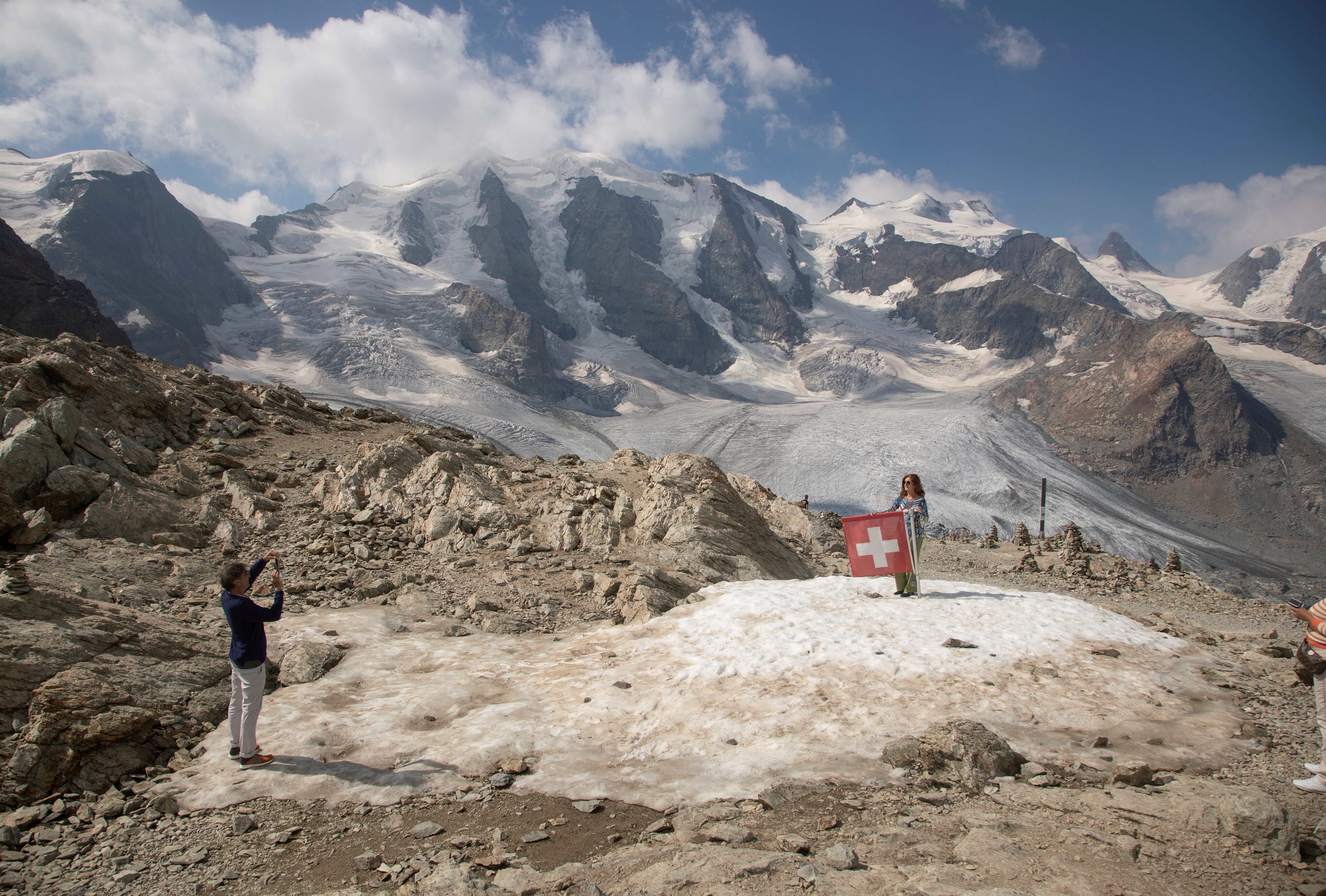A woman poses beside a Swiss national flag near a snow-topped mountain.