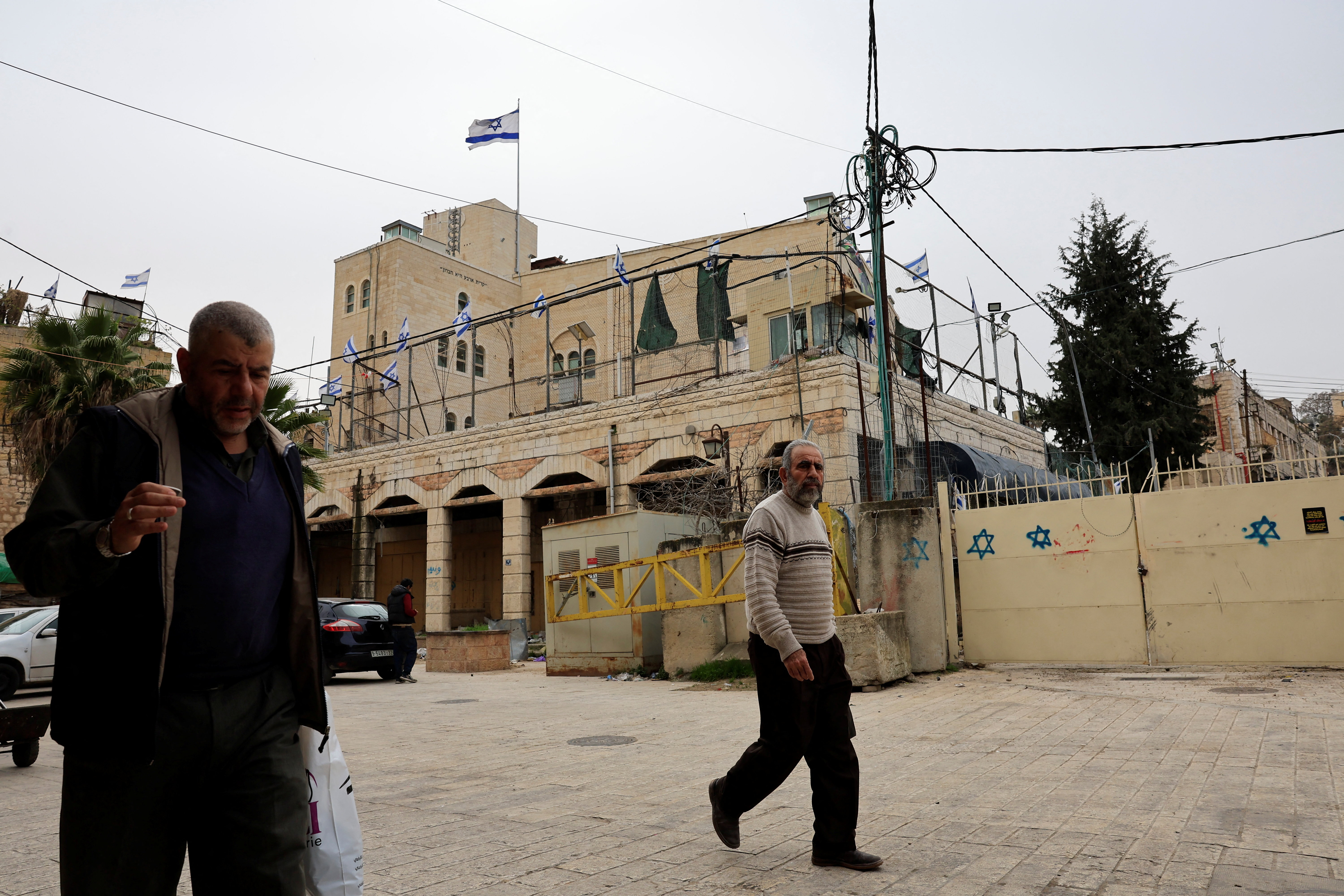 Palestinians walk in front of an Israeli settlement in Hebron