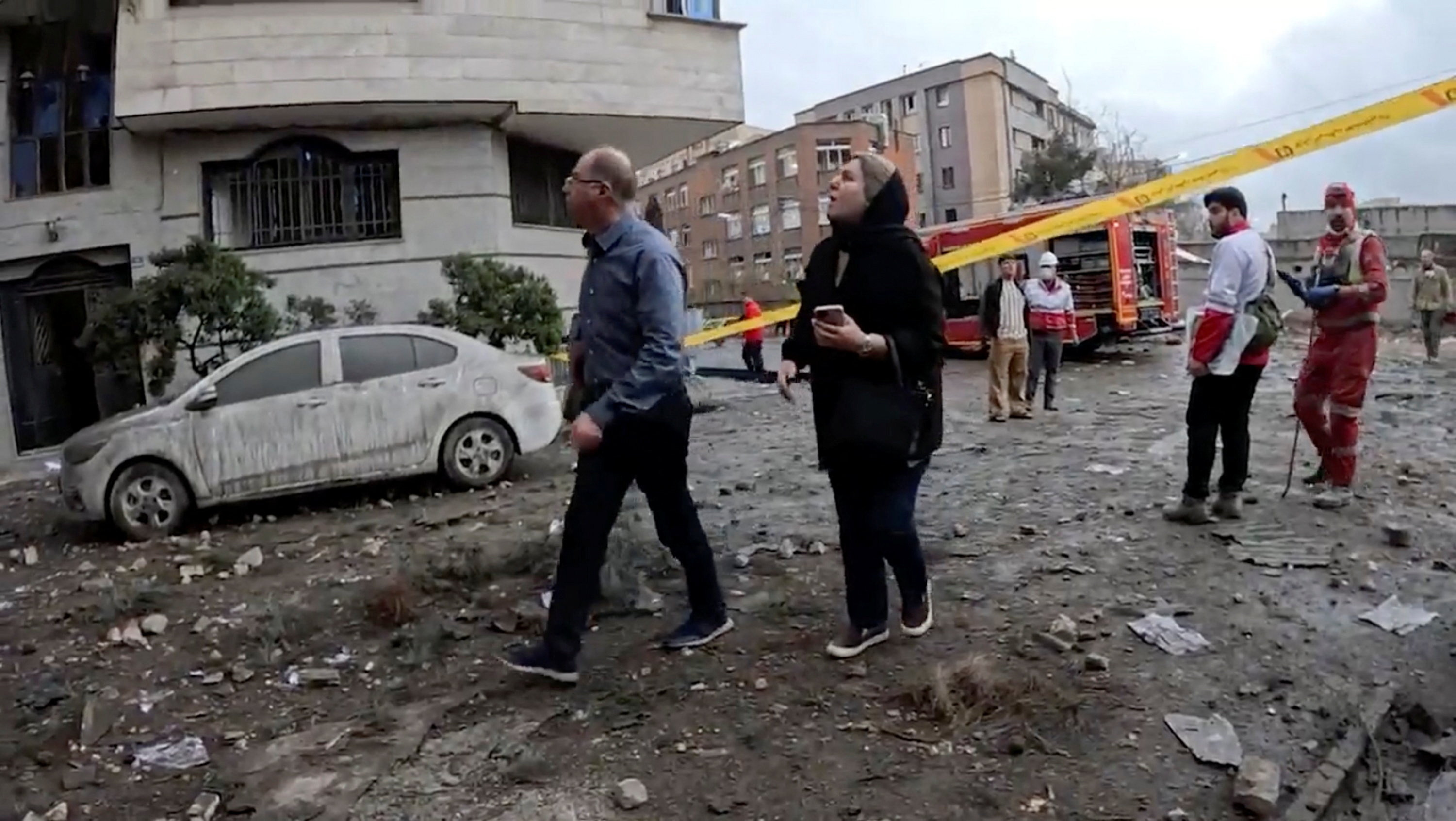 People walk near a cordoned off area, as members of the Iranian Red Crescent Society