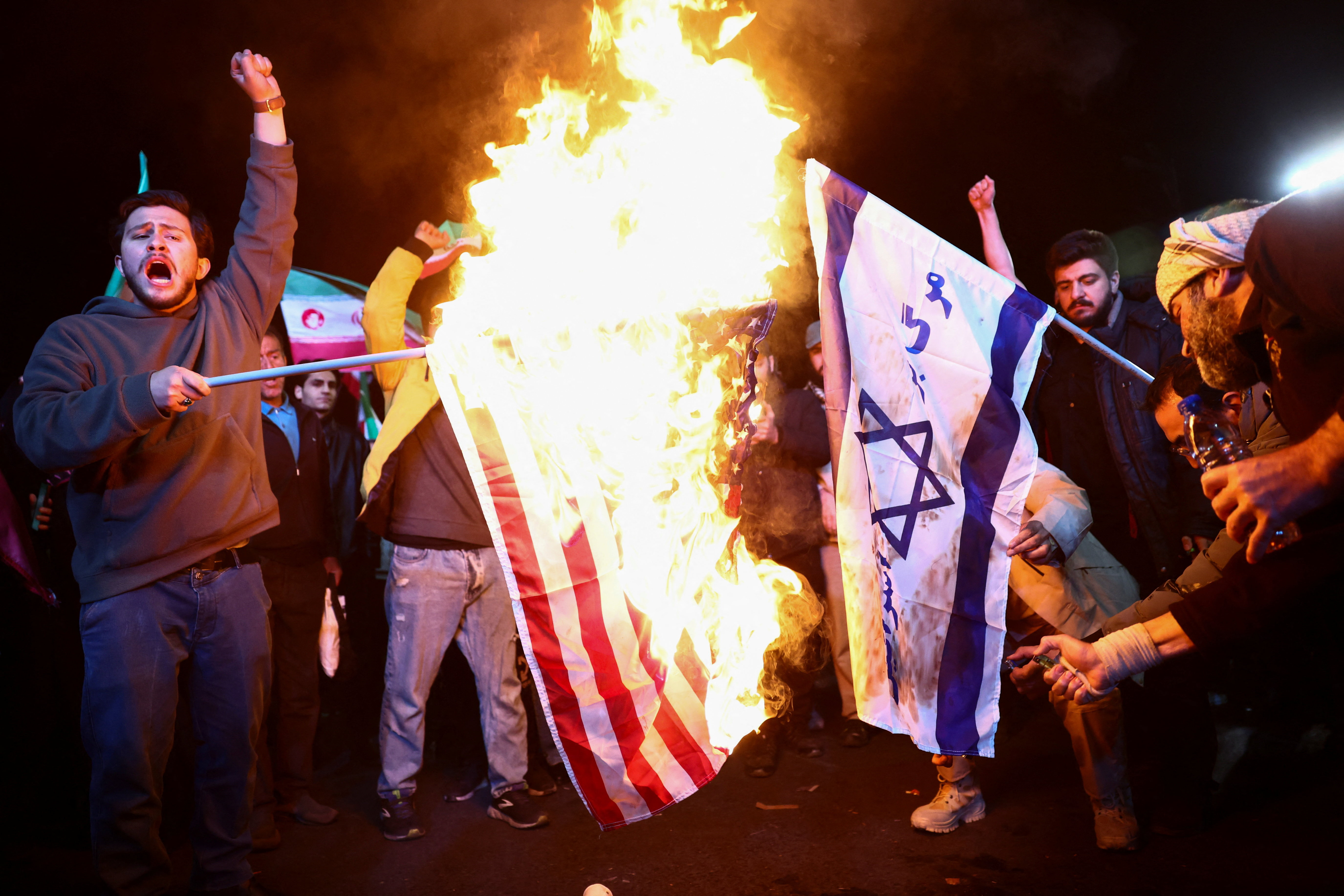 People burn the flags of the US and Israel in protest.