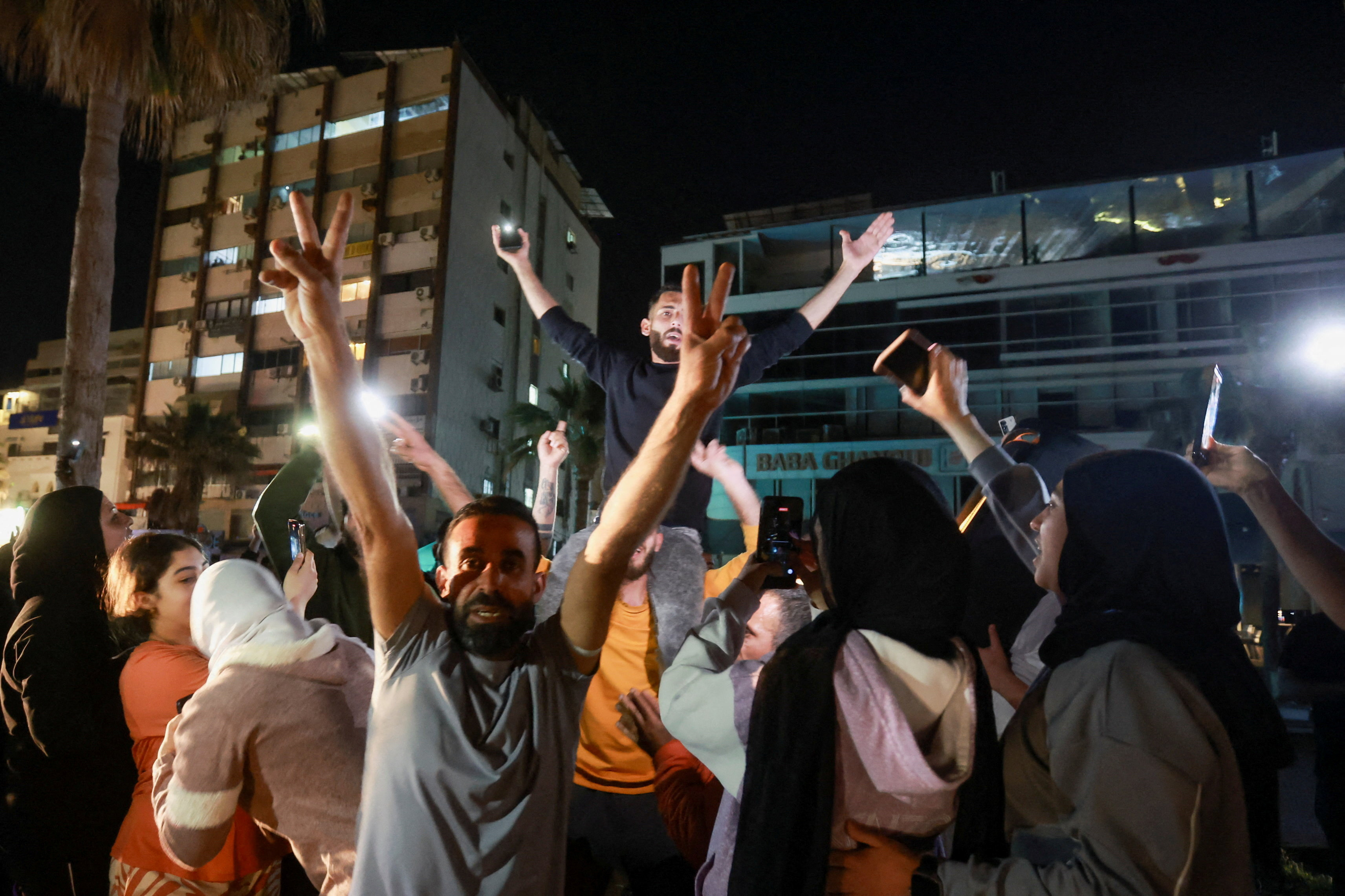 A crowd of people celebrate in front of some buildings in Sidon, Lebanon