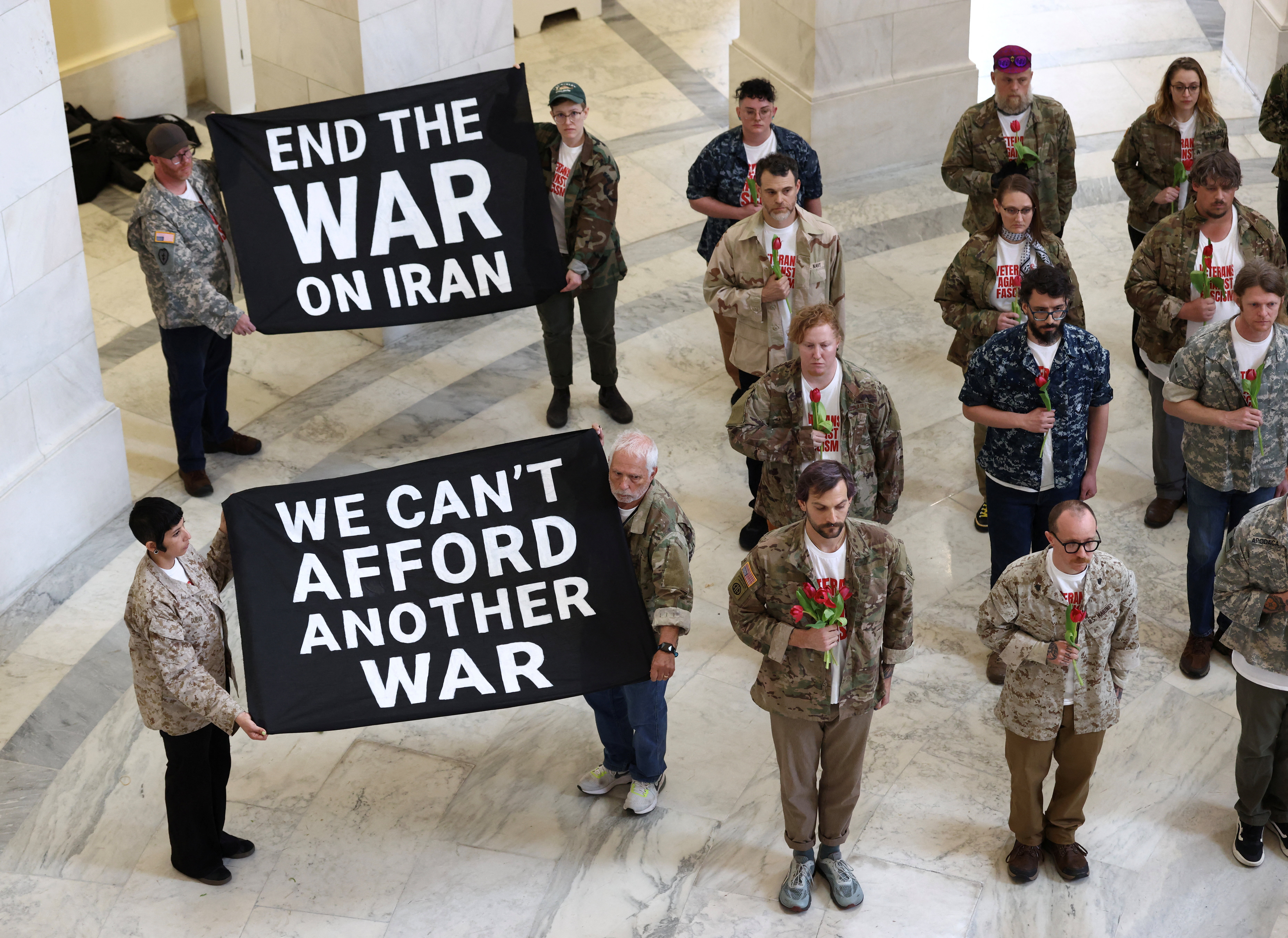 Clutching flowers to their chests, veterans with the group About Face and members of military families protest against the Iran war in the Cannon House Office Building Rotunda on Capitol Hill in Washington, D.C., U.S., April 20, 2026. [Kevin Lamarque/Reuters]