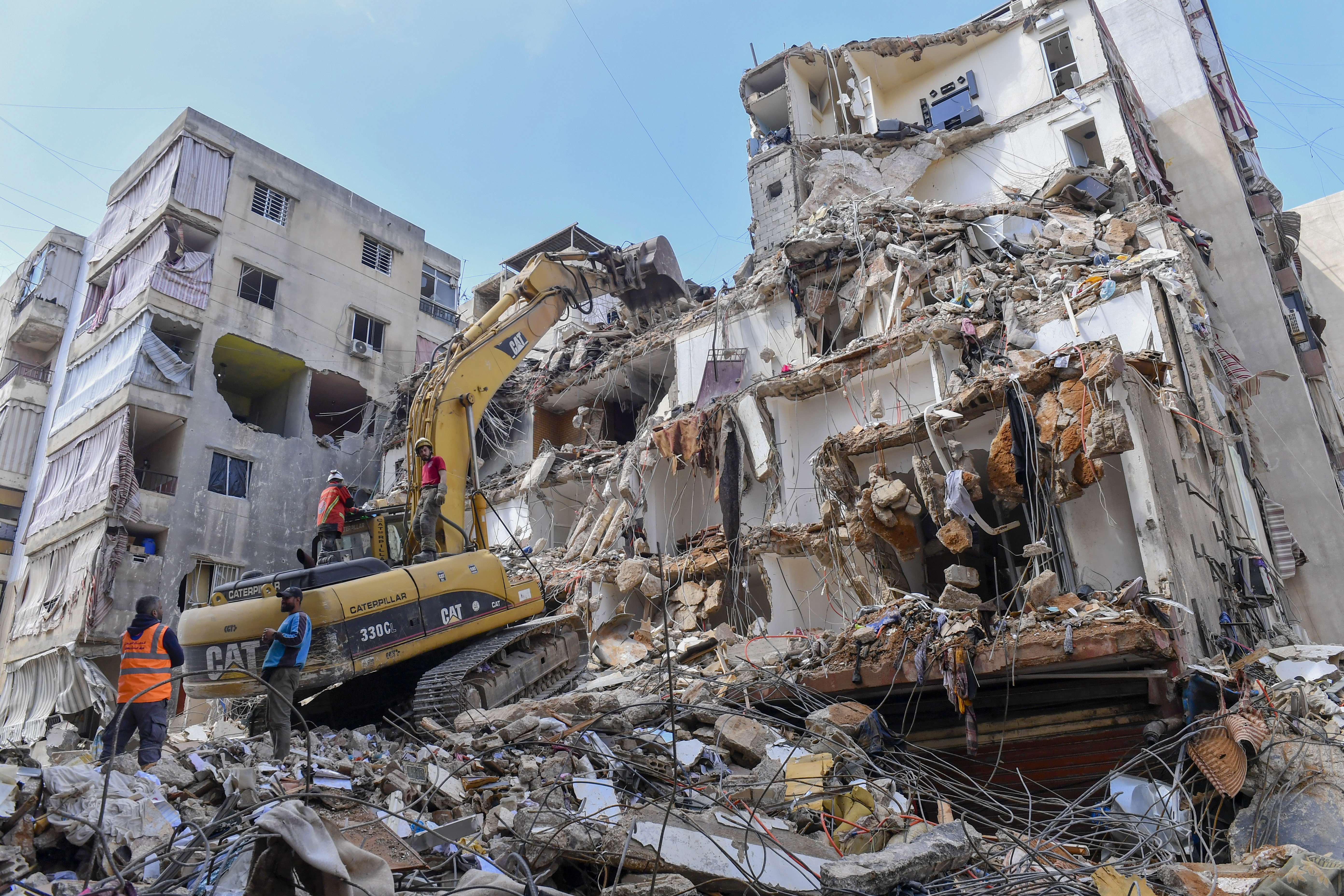 Civil defence workers and a bulldozer work at the site of a destroyed building.
