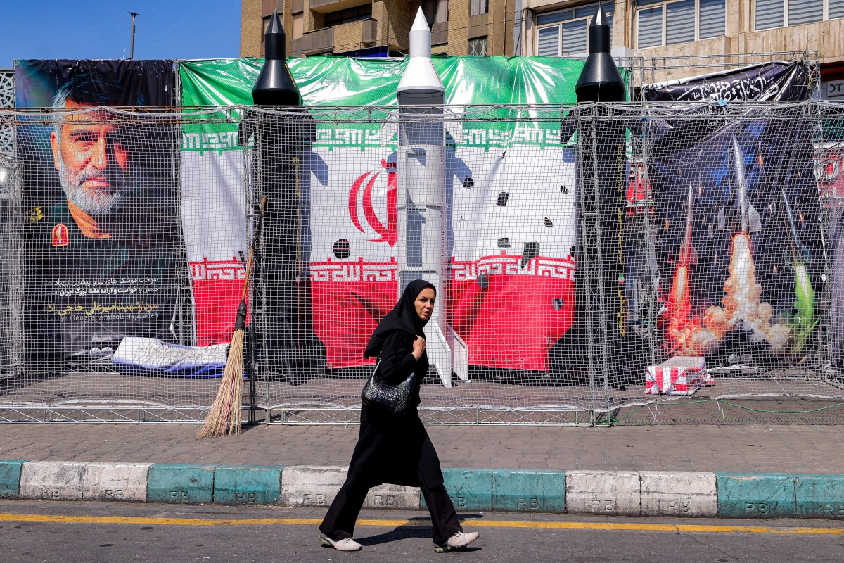 A woman walks past mockups of Iranian missiles along Valiasr Square in Tehran on April 6, 2026. Israeli strikes killed the intelligence chief of Iran's Revolutionary Guards, as the Islamic republic on April 6 defied threats from the US President to devastate civilian infrastructure if it does not reopen the Strait of Hormuz.