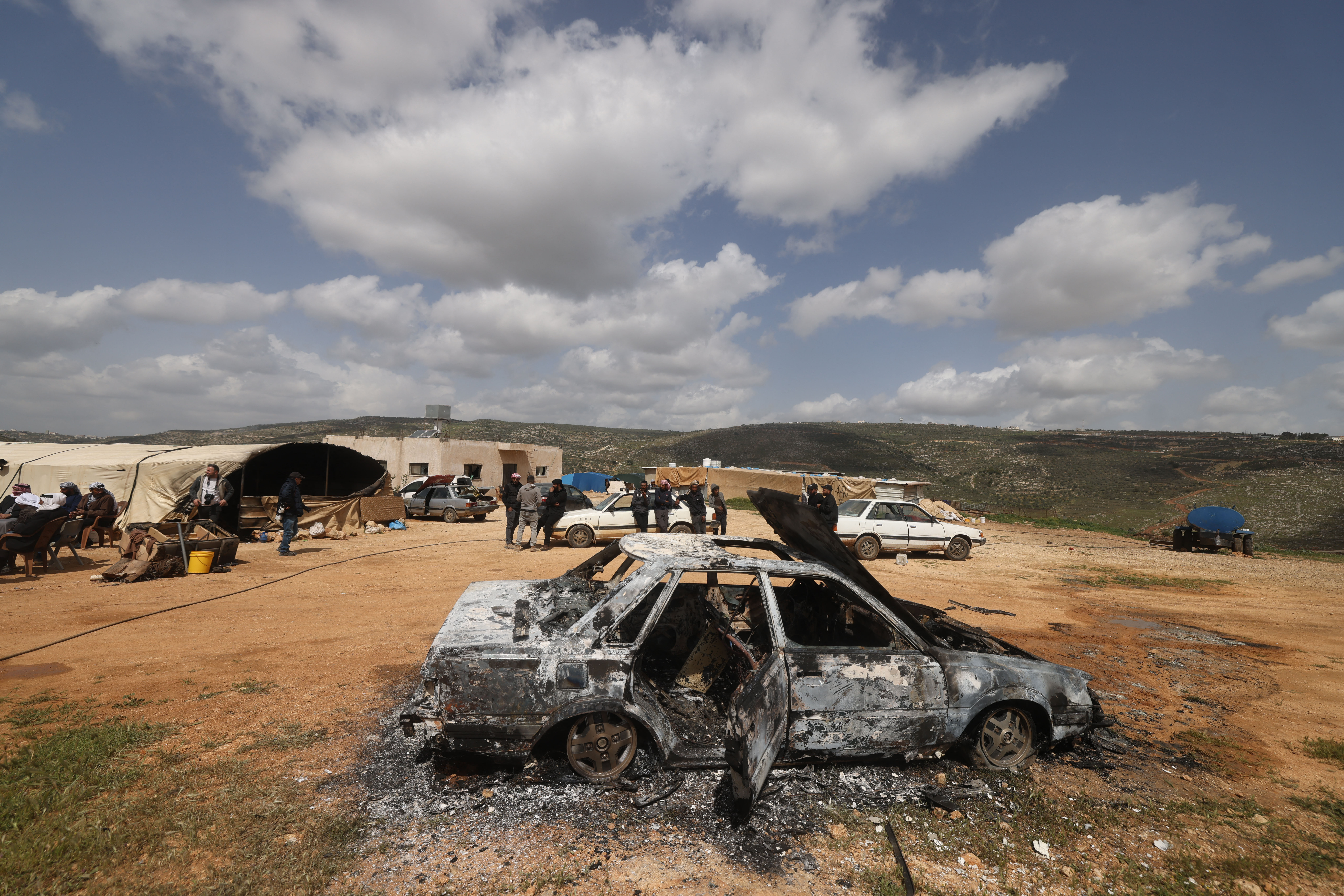Palestinians stand near a vehicle that was destroyed.