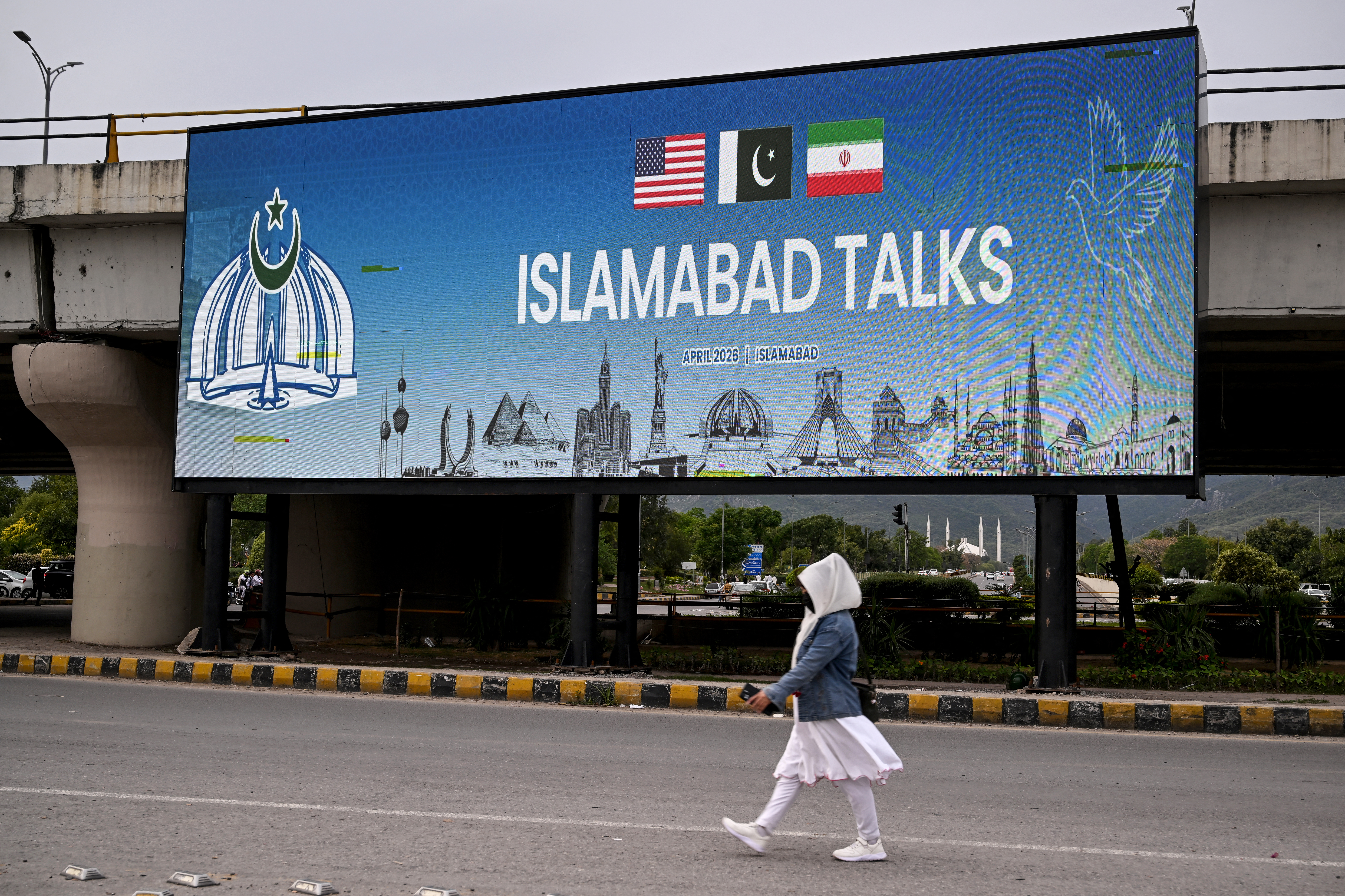 A woman walks past a digital screen displaying news of USIran peace talks along a road in Islamabad on April 10, 2026. A cloud of uncertainty hung April 10 over the scheduled start of talks in Pakistan between the United States and Iran, with no announcement yet on the arrival of negotiators and both sides accusing the other of failing to properly implement a fragile ceasefire. (Photo by Farooq NAEEM / AFP)