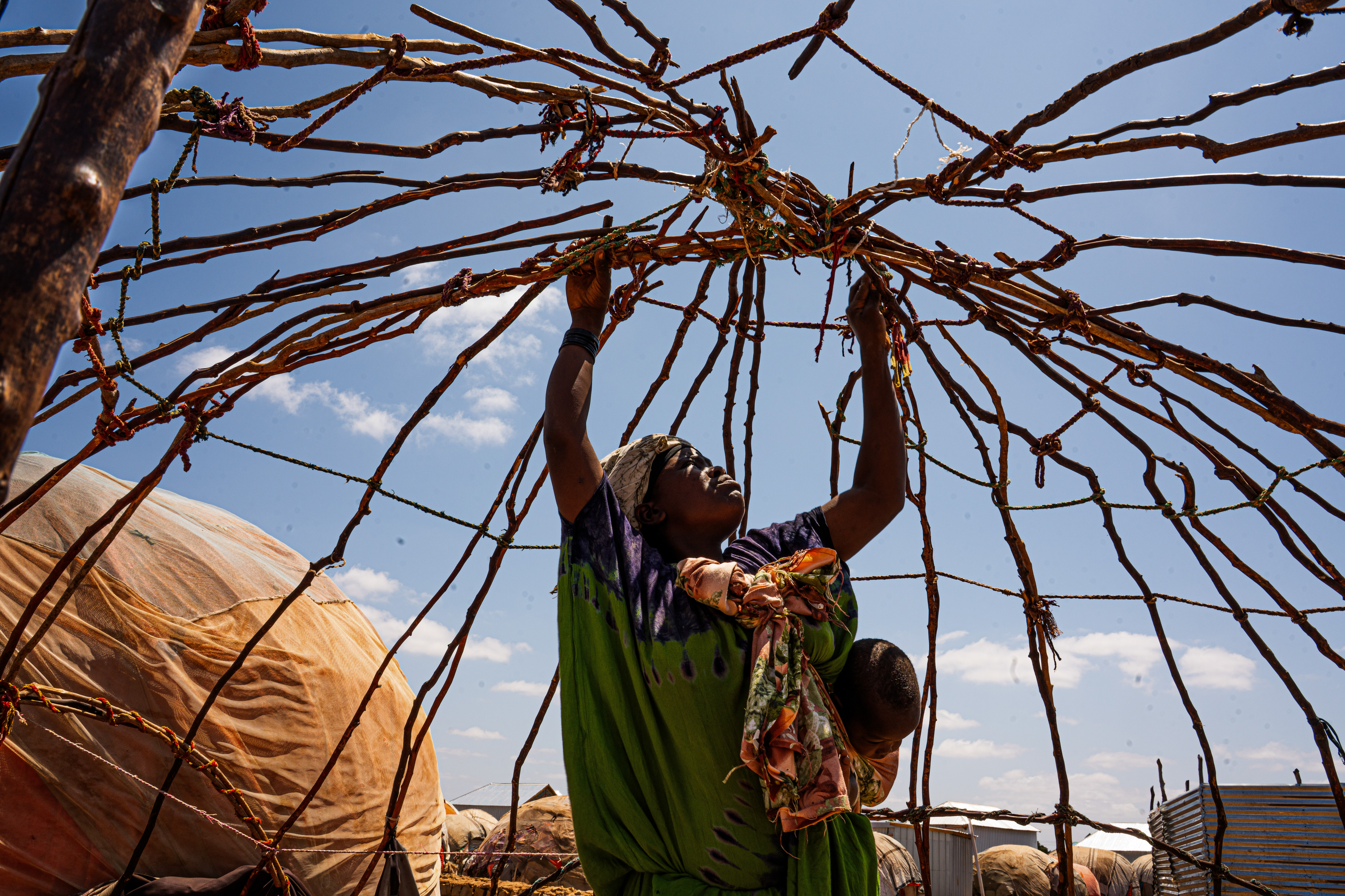 Shukri Adan Hassan, 23, and her six children fled Wajid after losing all their livestock in the September drought and arrived in Baidoa seeking refuge. She is building a temporary shelter at Qaydar-adde camp with whatever materials she can find. Since arriving, the family has not received any humanitarian assistance. Qaydar-adde displacement camp, Baidoa, Southwest State, Somalia. [Abdulkadir Mohamed/NRC]