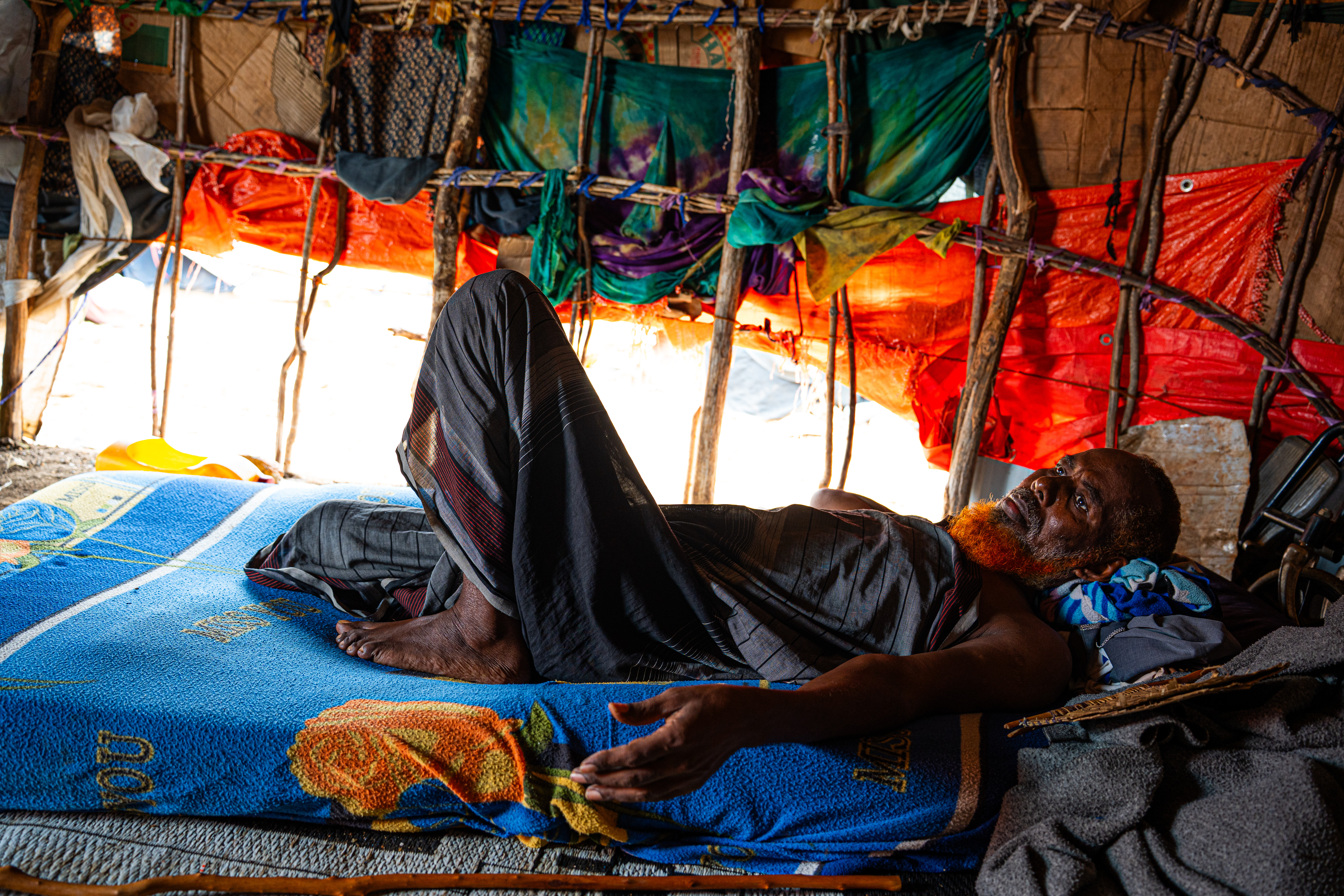 Mohamed Ganey is 63 years old, disabled, and living with high blood pressure. When drought destroyed his family's livestock in the Bakool region, he was too weak to walk. His children carried him on a donkey cart for several days with little food or water before reaching Baidoa. At the displacement camp, he has no access to food and cannot afford the medicine he needs. He spends most of his time lying in a temporary shelter, waiting for his children to return. Some days, they come back with nothing. Baidoa, Southwest State, Somalia. [Abdulkadir Mohamed/NRC]