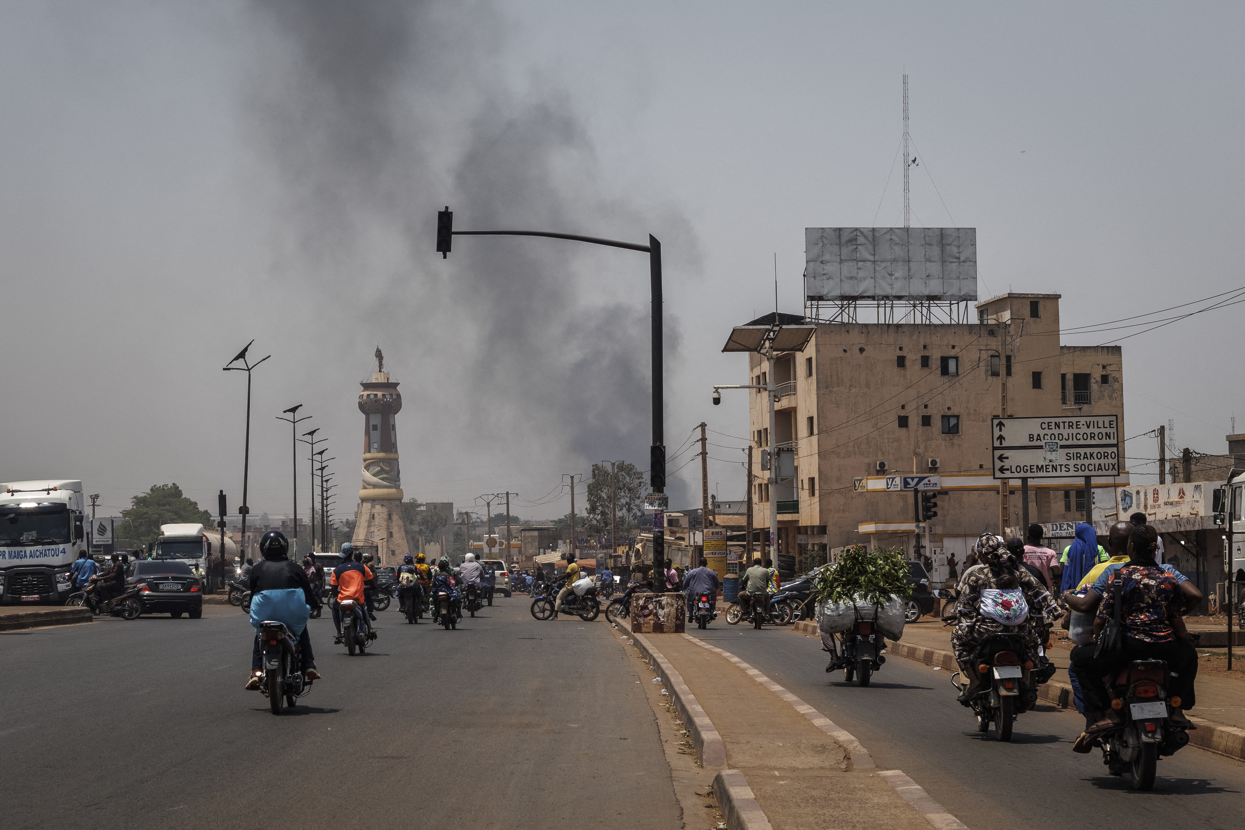 TOPSHOT - A column of black smoke rises above buildings as traffic passes the Africa Tower monument in Bamako on April 26, 2026.