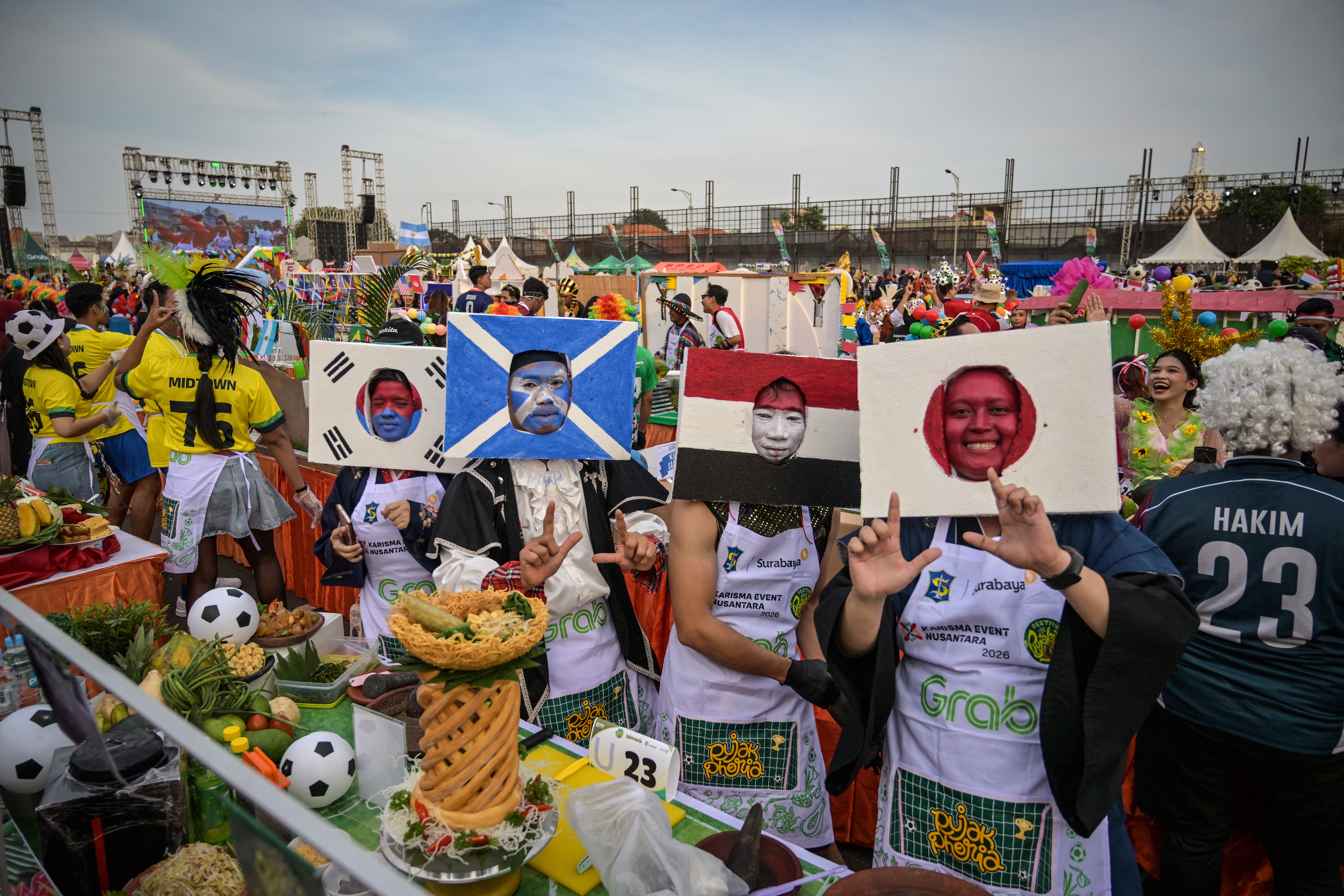 Participants dressed in football team national flags dance before preparing rujak uleg, a traditional Indonesian savoury salad that features beef muzzle and vegetables, during the "History of Rujak Uleg Festival" to welcome the upcoming 2026 FIFA World Cup in Surabaya on May 9, 2026. (Photo by JUNI KRISWANTO / AFP)