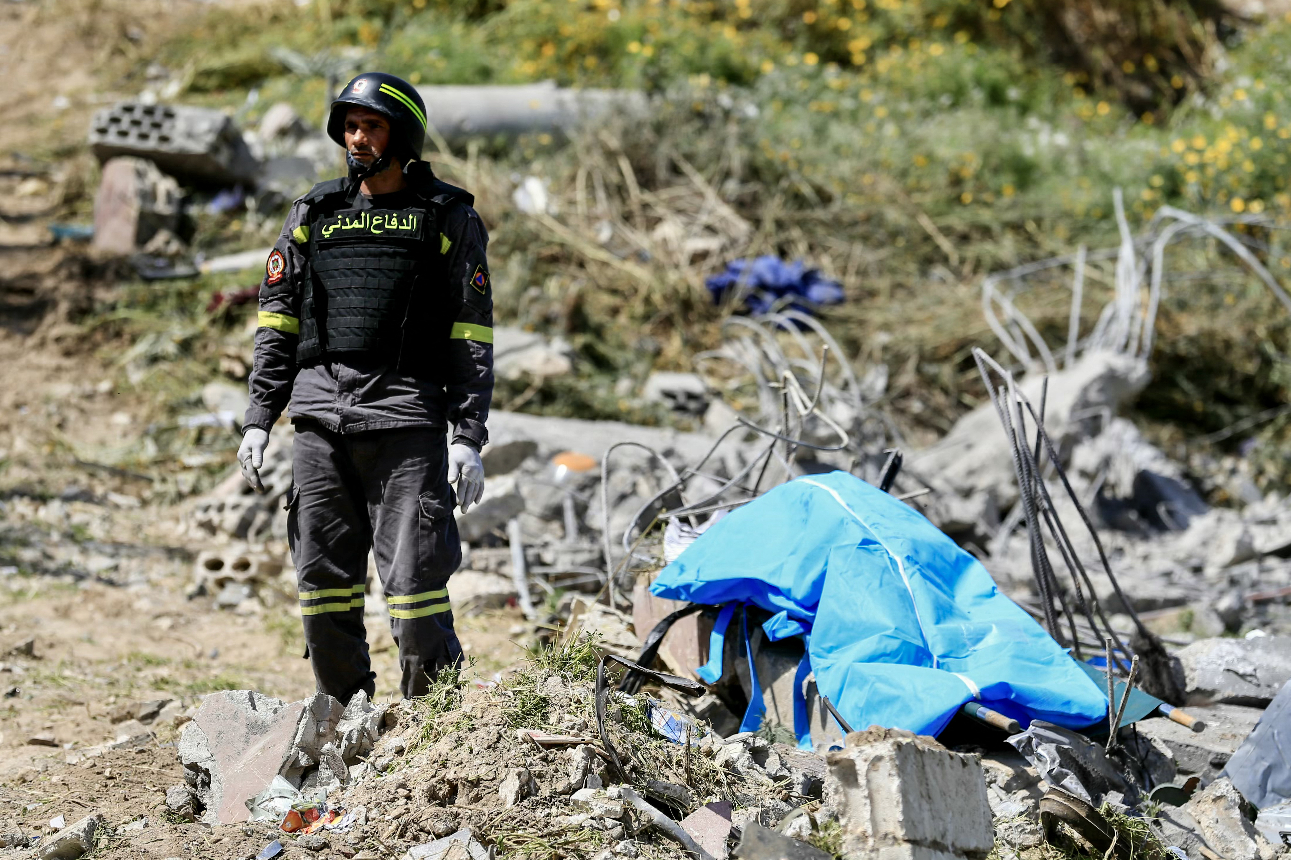A first responder stands by a body bag as colleagues search the rubble for victims at the site of an Israeli airstrike in the southern village of Saksakieh on May 9, 2026.