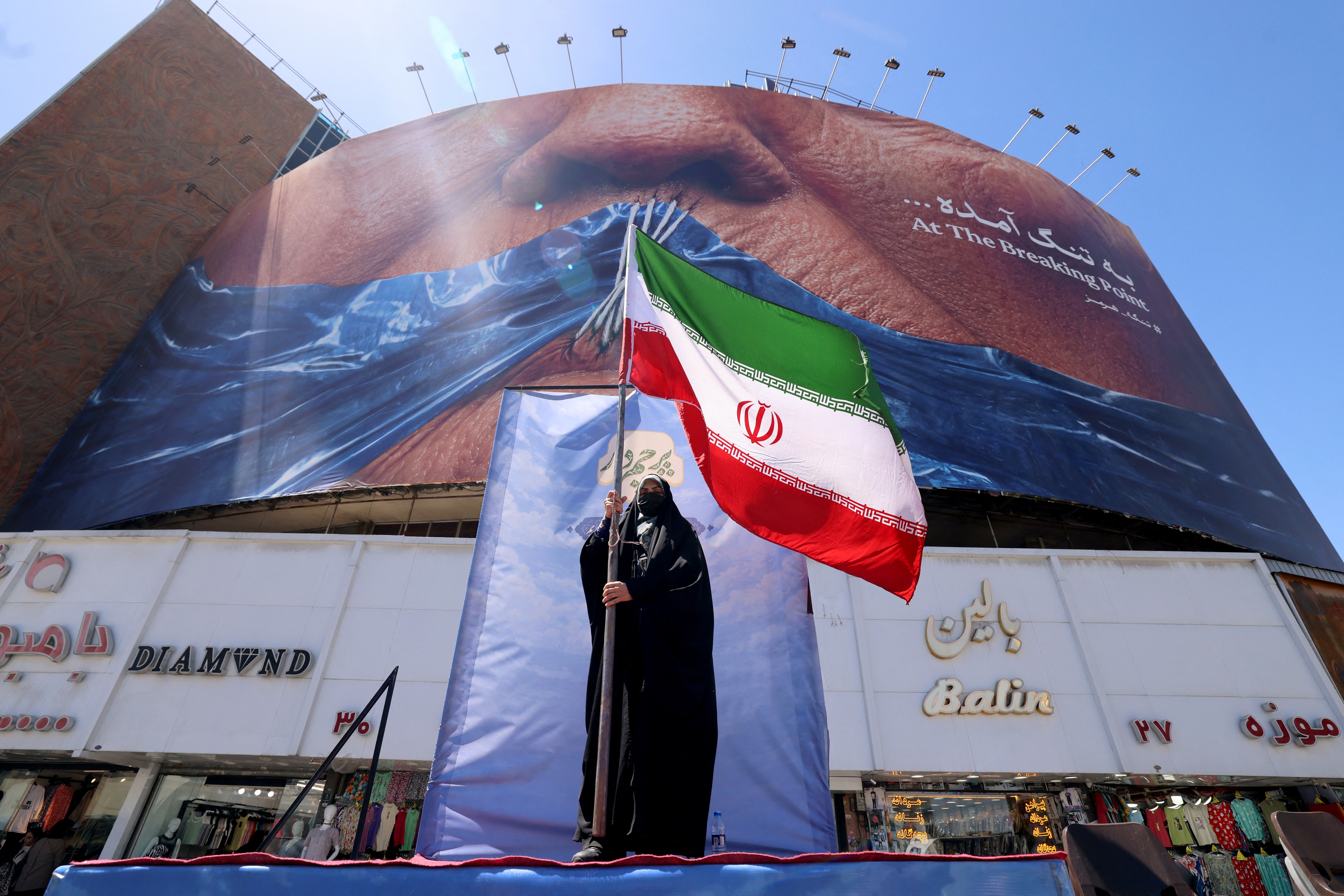 A woman holds the Iranian flag as she stands infront of an anti-US billboard referring to President Donald Trump and the Strait of Hormuz, installed on a building at the Valiasr Square in Tehran on May 10, 2026.