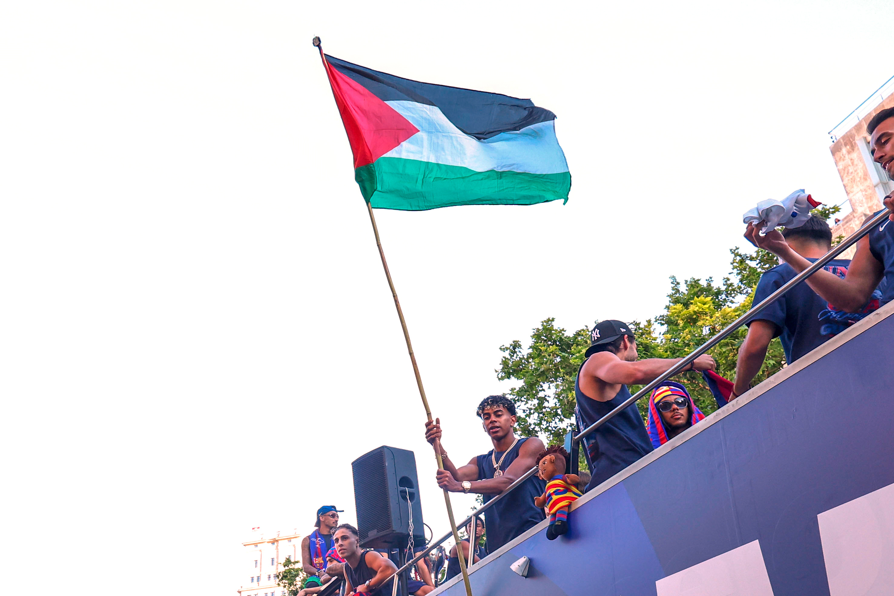 FC Barcelona player Lamine Yamal holds a Palestinian flag as he celebrates with his team atop a bus after winning the Spanish La Liga title in Barcelona