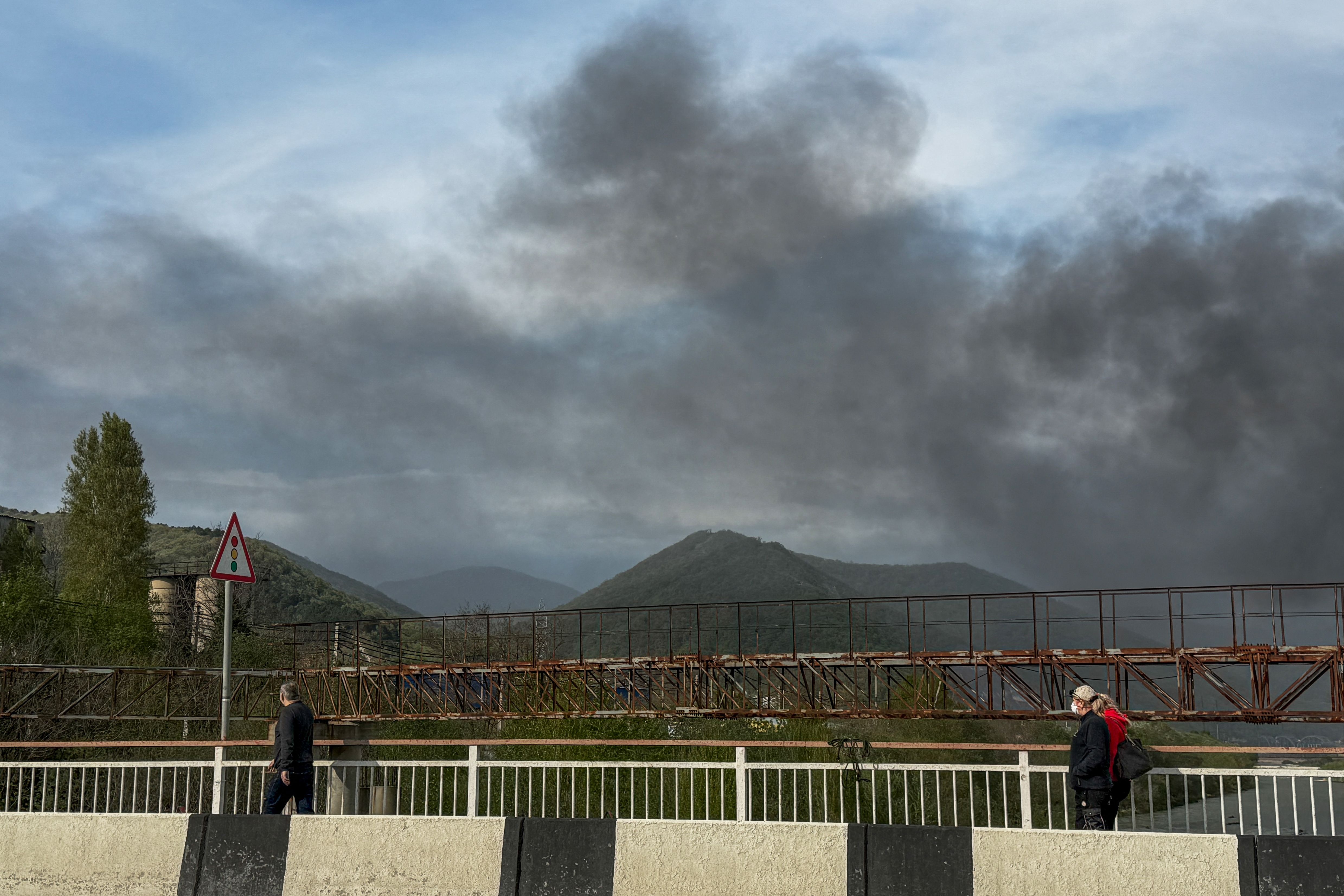 Pedestrians walk across a bridge as smoke rises following a recent drone attack on the Tuapse oil refinery in Tuapse, Krasnodar region on April 29, 2026, amid the ongoing Russian-Ukrainian conflict.