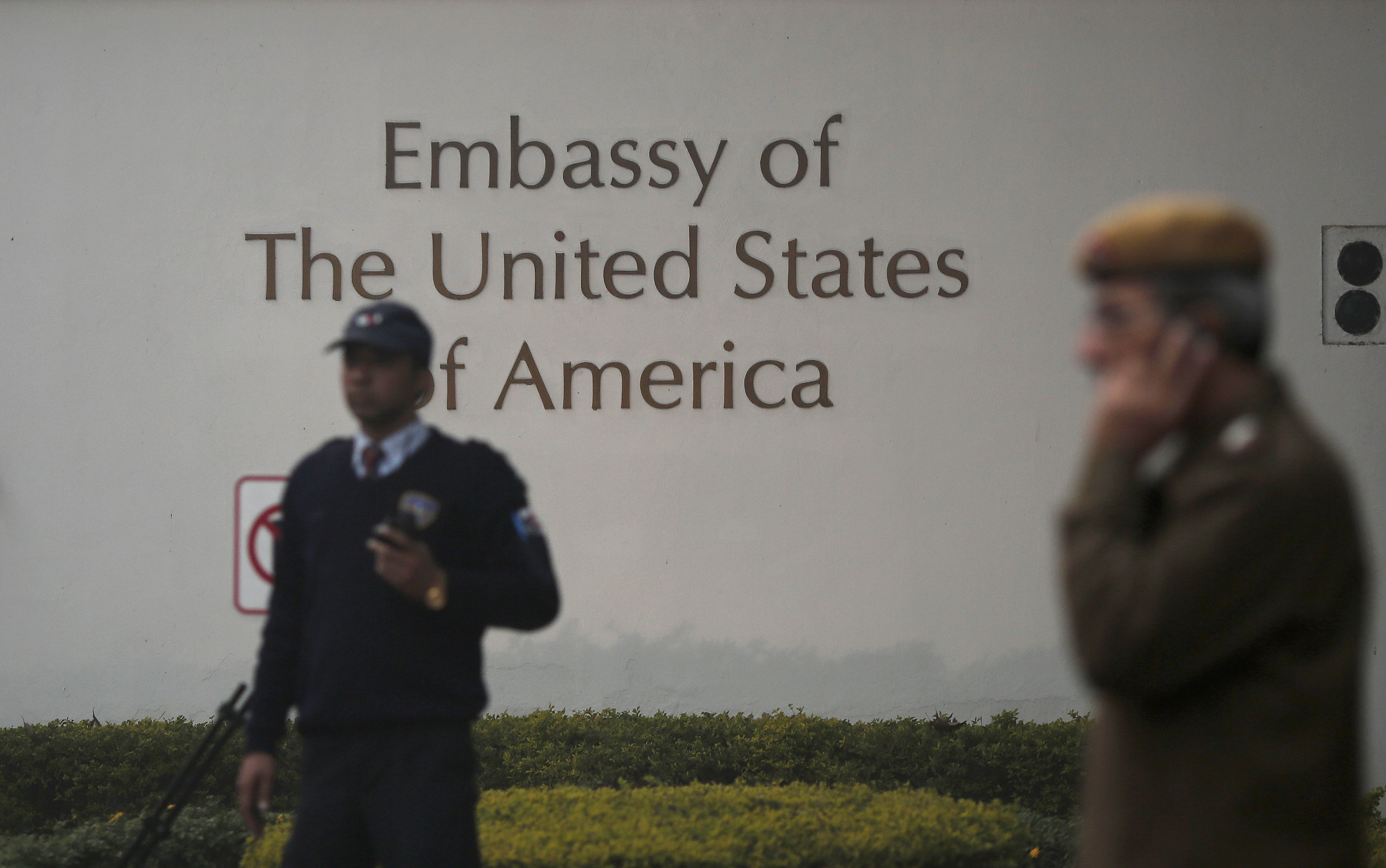 A U.S. embassy security guard (L) and an Indian policeman stand in front of the main gate of the embassy as the bulldozer (unseen) removes the security barriers, in New Delhi