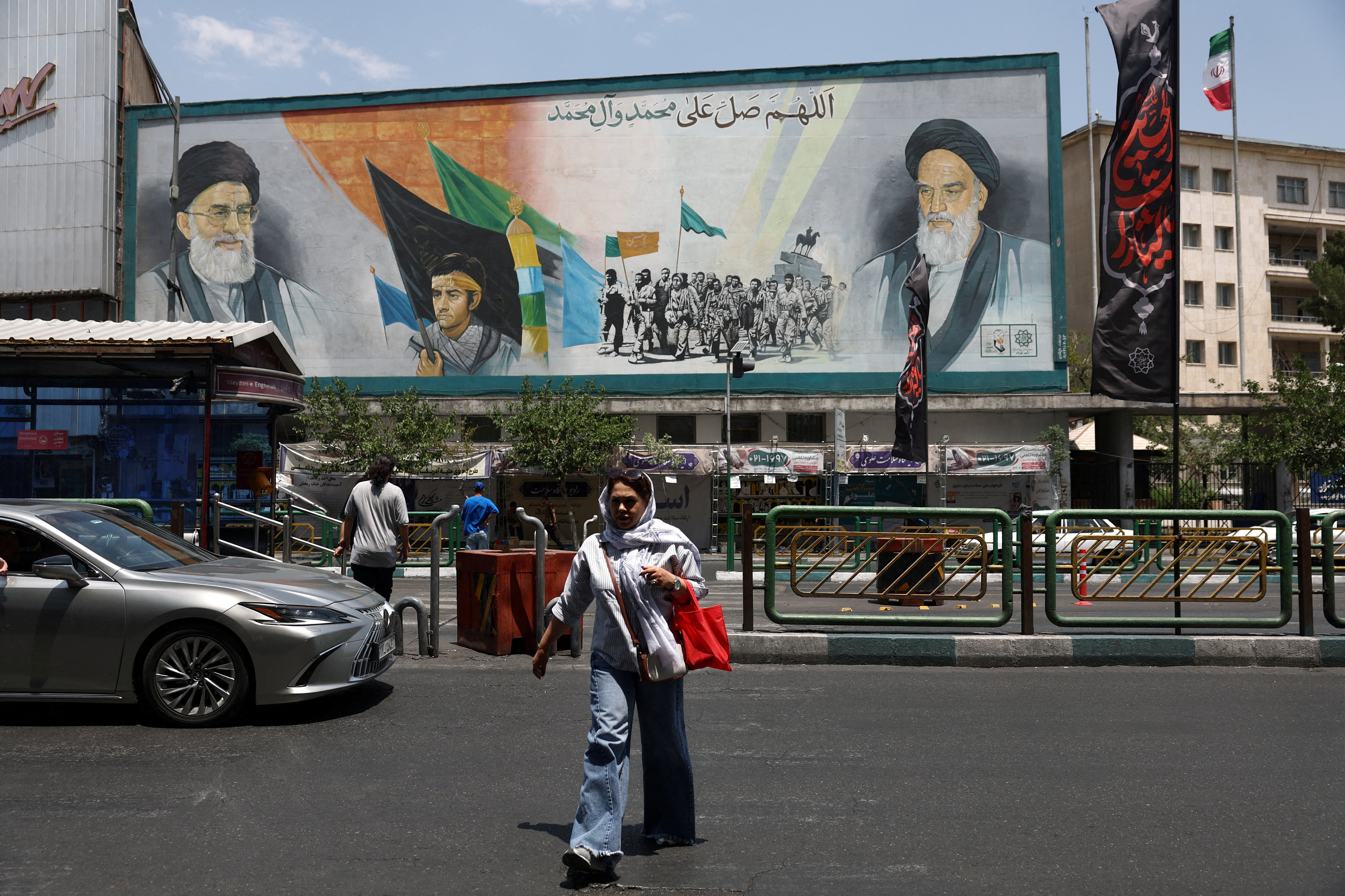 A billboard in a Tehran street displays large portraits of Ayatollah Ruhollah Khomeini and Ayatollah Ali Khamenei as people pass by below.