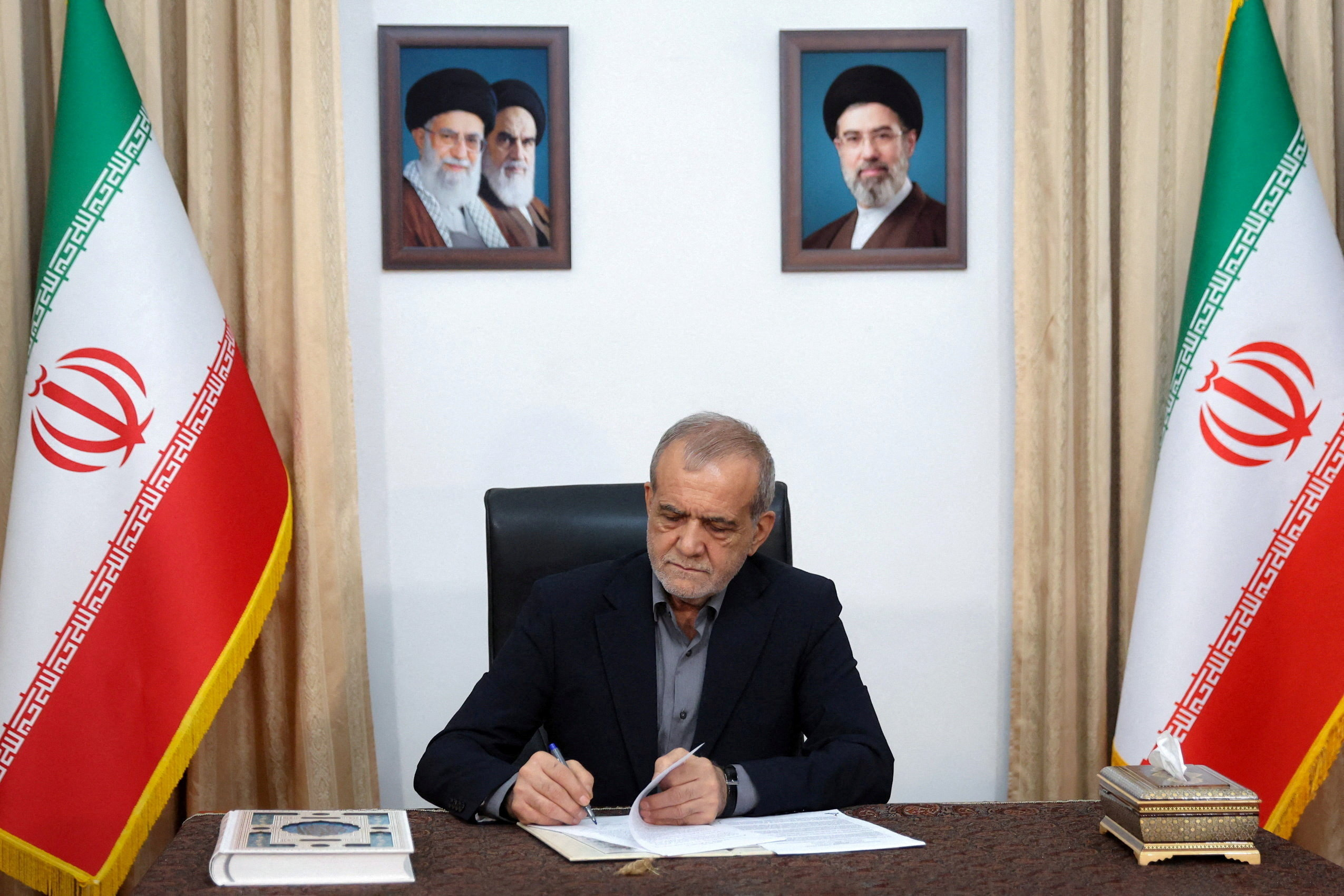 Iranian President Masoud Pezeshkian signs a document.