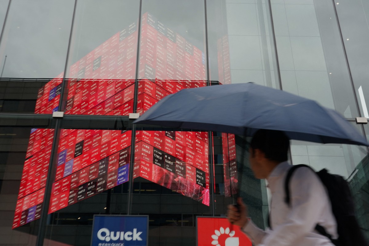 A man walks in front of an electronic quotation board displaying stock prices.