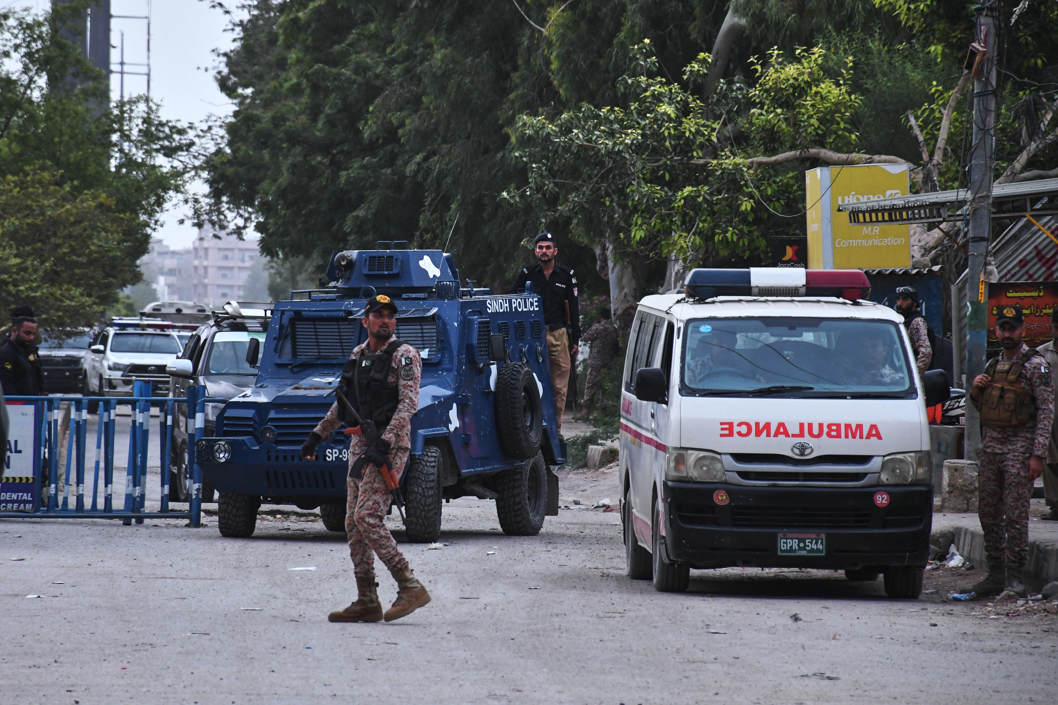 Armed paramilitary soldiers and police officers stand guard on a cordoned-off road, with buildings visible behind them