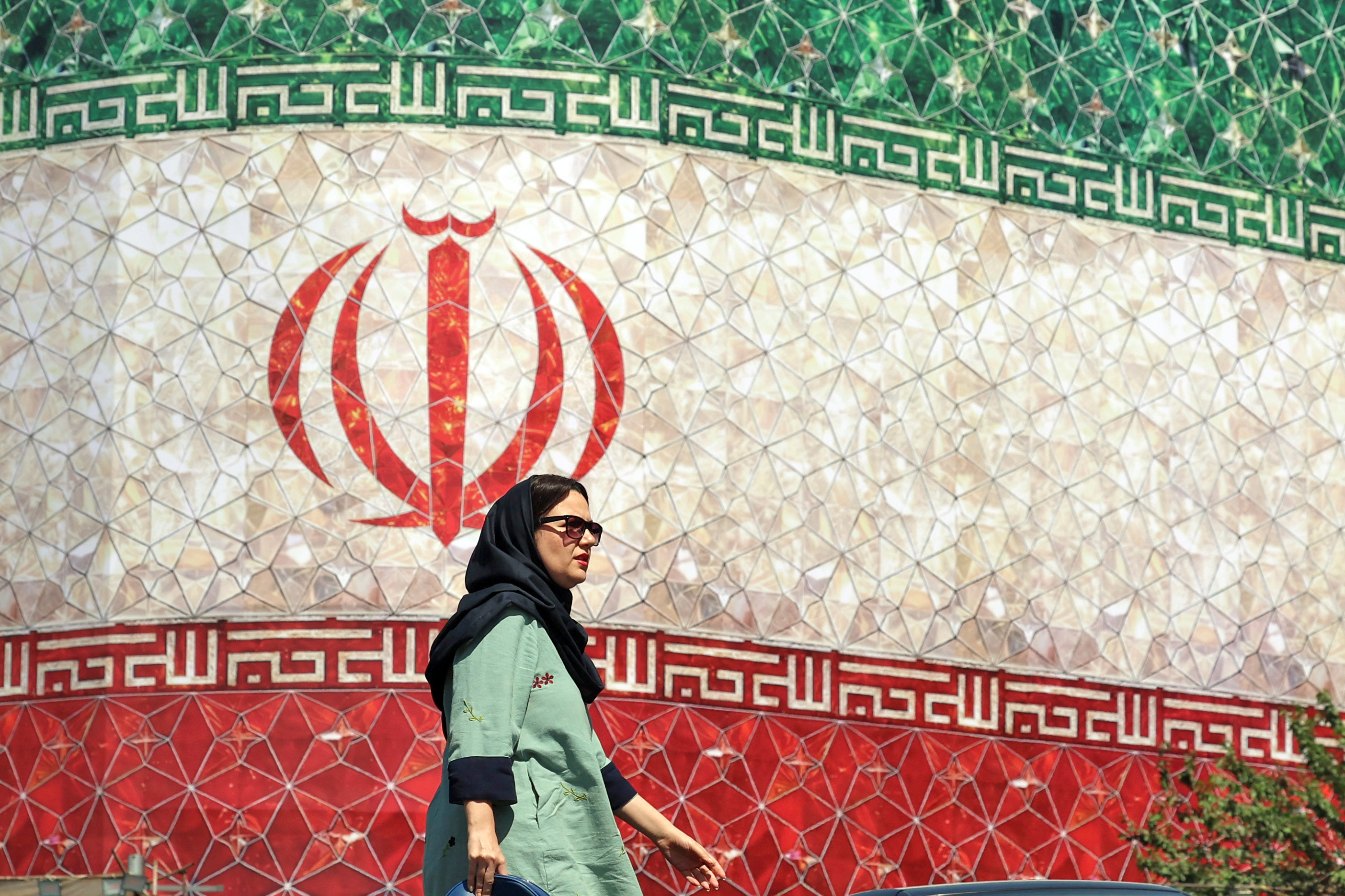 A woman walks past a billboard displaying Iran’s national flag.