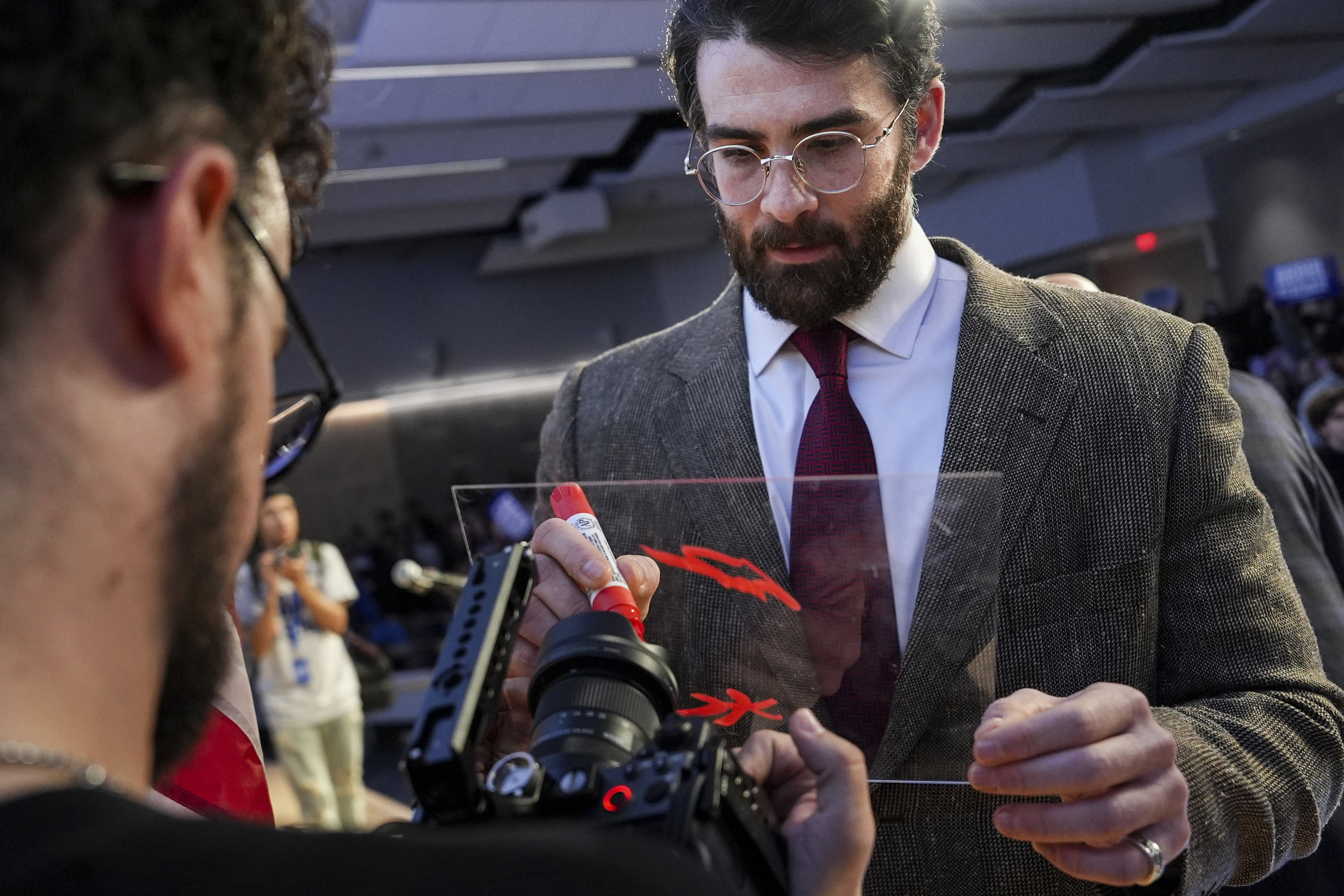 Streamer Hasan Piker signs a panel in front of a camera lens during a campaign event for Abdul El-Sayed, a progressive candidate in the Democratic primary for U.S. Senate in Michigan, Tuesday, April 7, 2026, at the University of Michigan in Ann Arbor, Mich. (AP Photo/Julia Demaree Nikhinson)