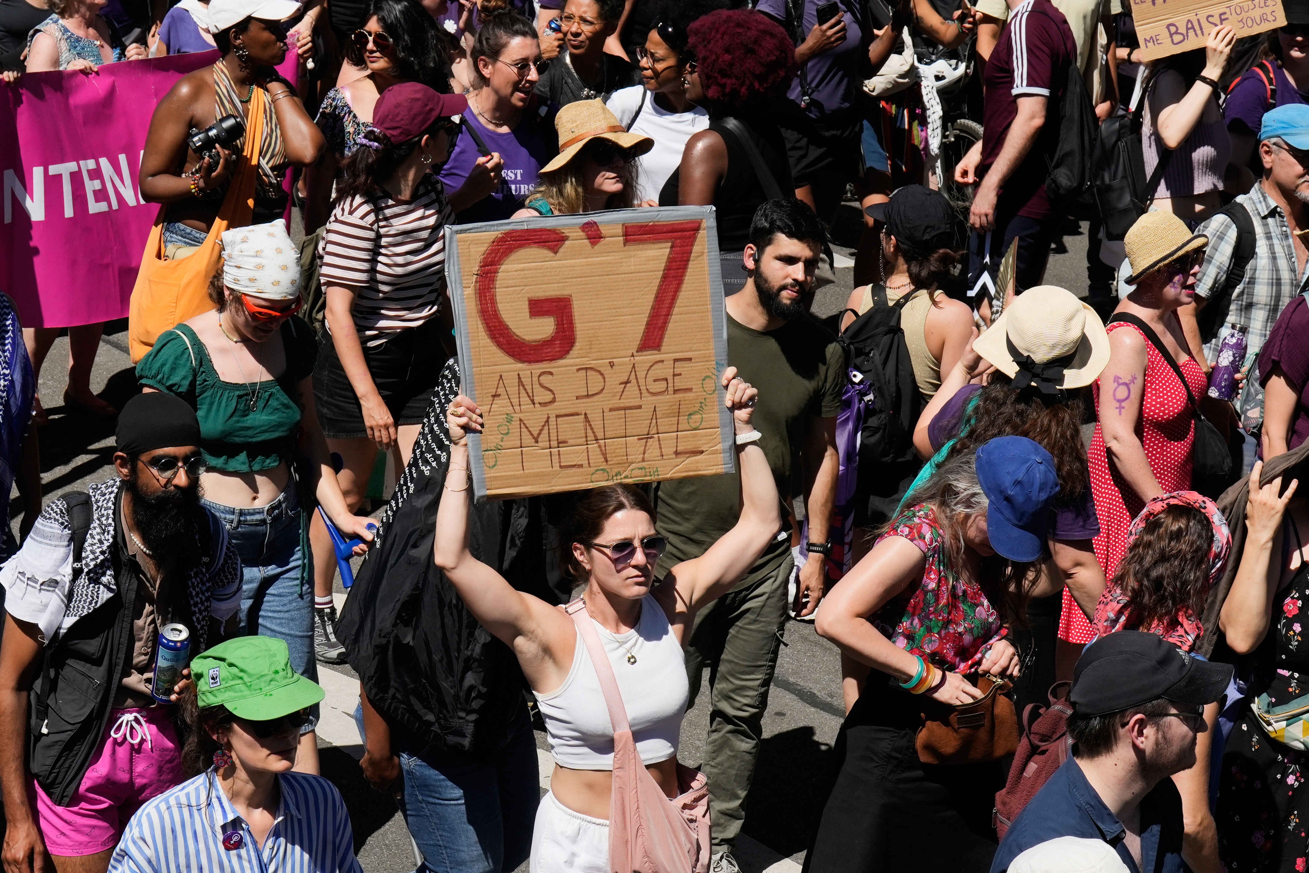 A woman holds a sign which reads "G7-mental age years" as she participates in a "No G7" demonstration in Geneva, Switzerland, Sunday, June 14, 2026, ahead of the G7 summit scheduled to take place June 15-17. (AP Photo/Baz Ratner)