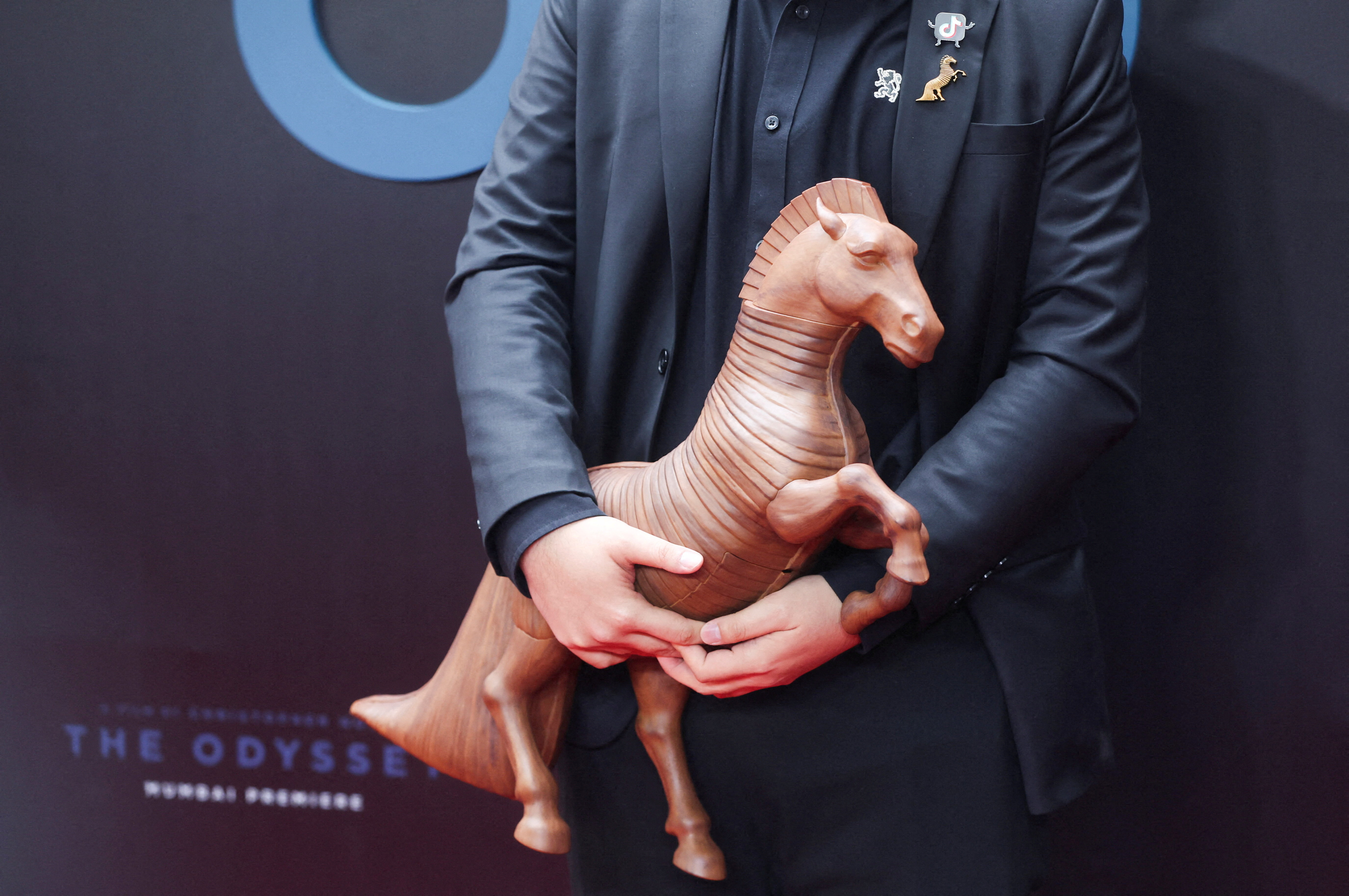 A social media influencer holds a replica of a horse on the red carpet during the Mumbai premiere of The Odyssey, in India