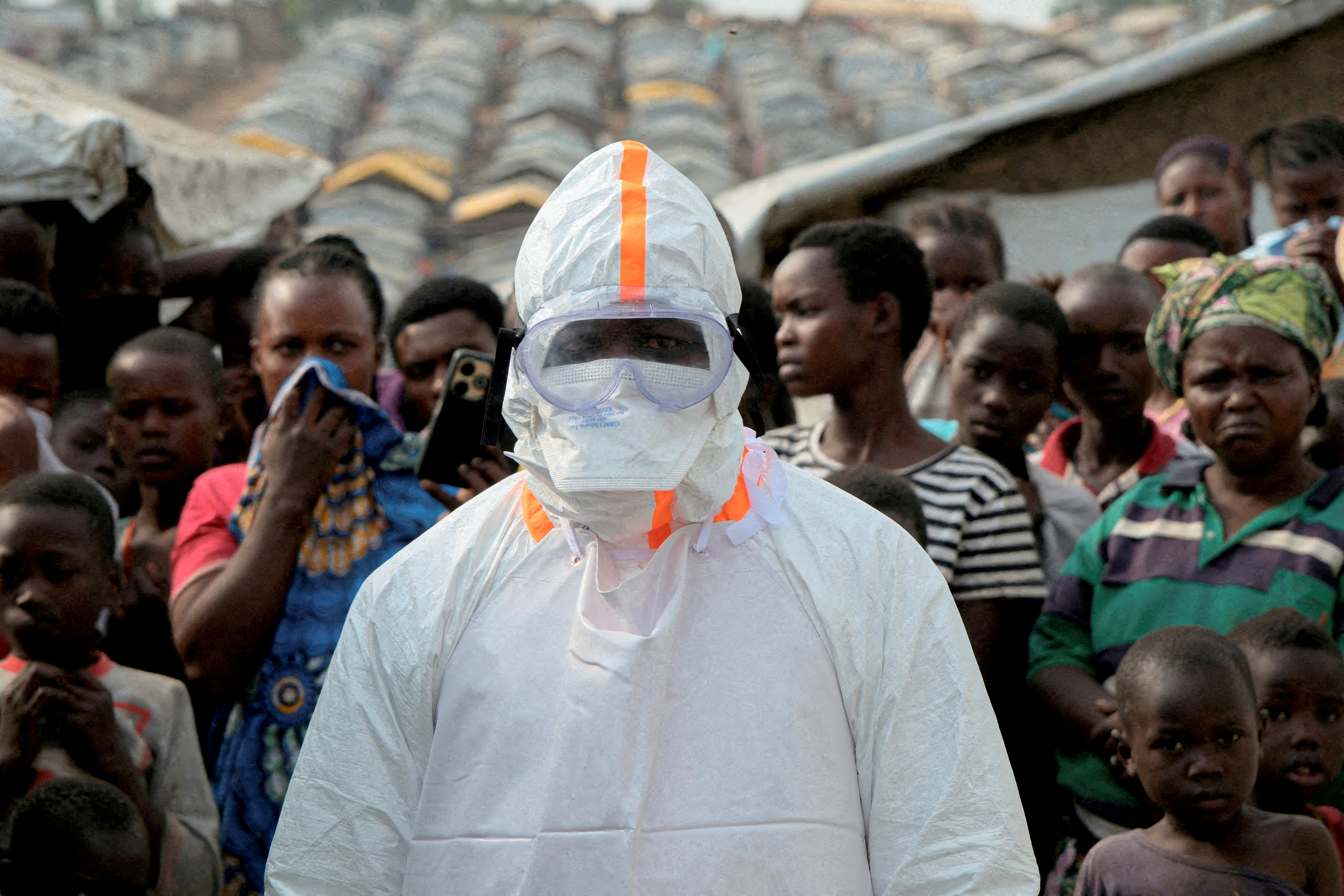 FILE PHOTO: FILE PHOTO: A health worker in personal protective equipment stands near displaced people waiting for the burial of suspected Ebola victims at the Kigonze displaced persons camp, one month after an outbreak was declared, in Bunia, eastern Democratic Republic of Congo, June 18, 2026. REUTERS/Gradel Muyisa Mumbere//File Photo/File Photo