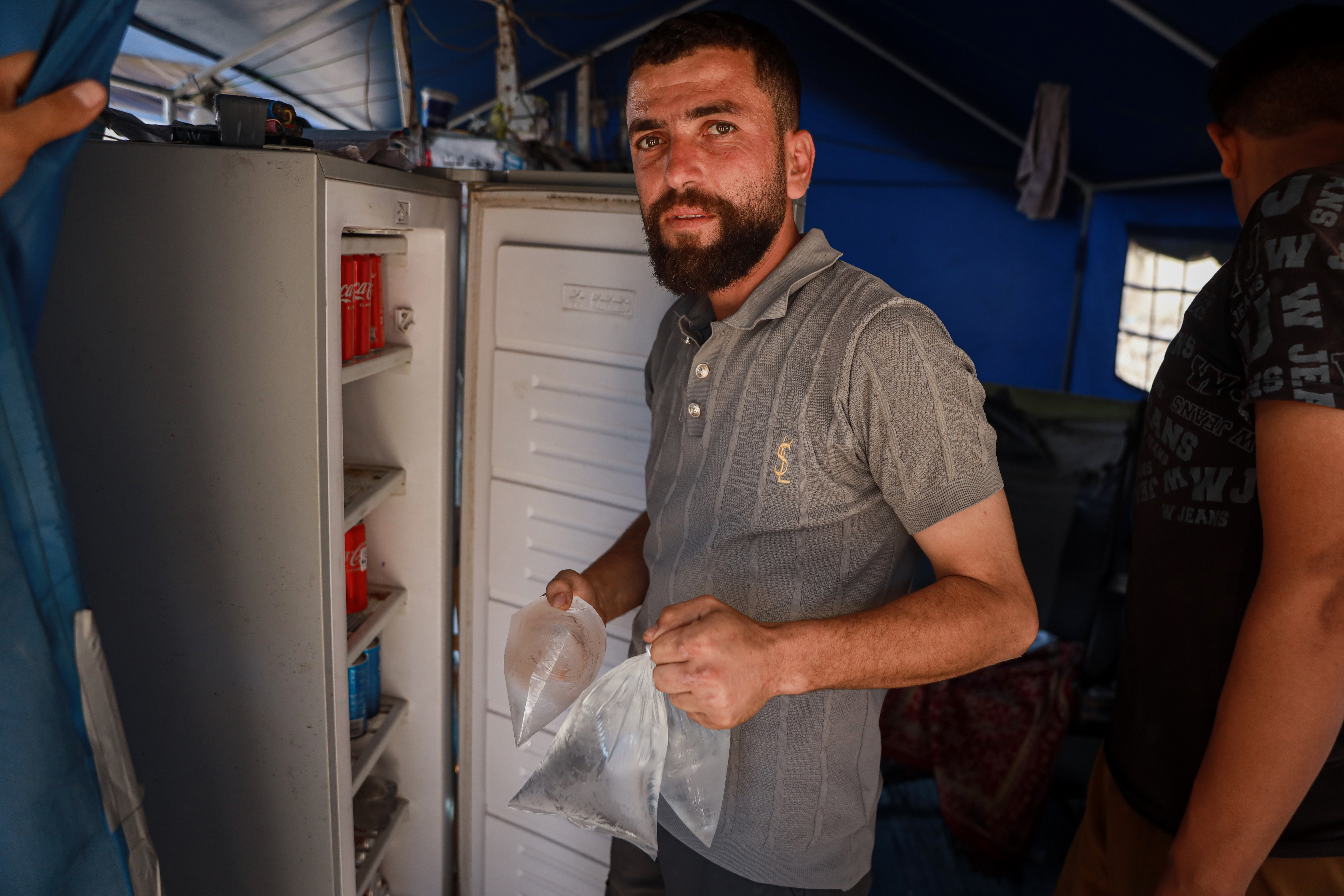 Mohammad Al-Zaanin runs a freezer service in a camp in central Gaza City, cooling water bags, drinks and other items for displaced families for a fee [Abdelhakim Abu Riash/ Al Jazeera]