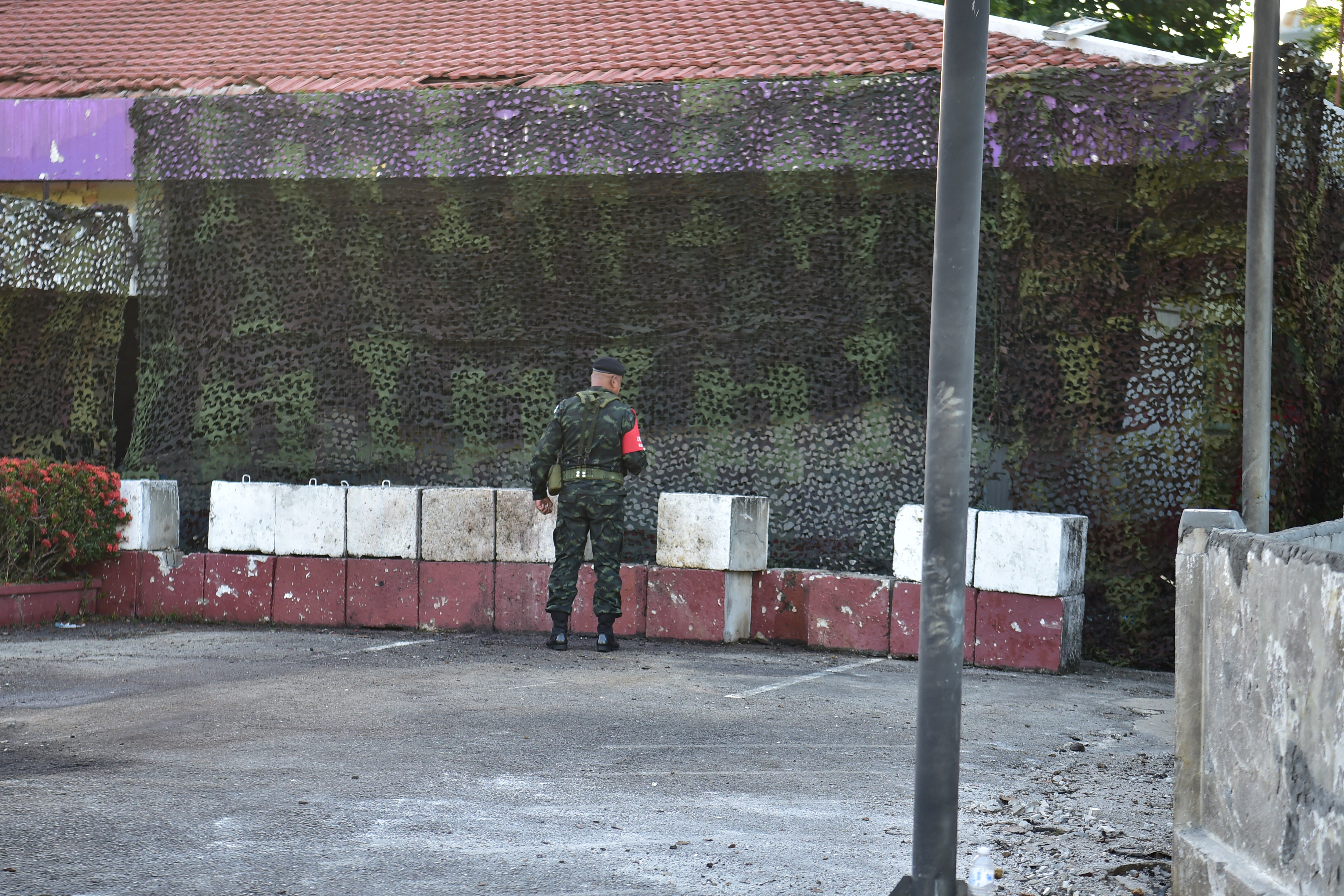A security official looks on in front of barriers and camouflage netting covering the damaged old Khao Tanyong police station in Thailand's southern province of Narathiwat on July 22, 2026, after an explosive device planted on a car was detonated overnight. (Photo by Madaree TOHLALA / AFP)