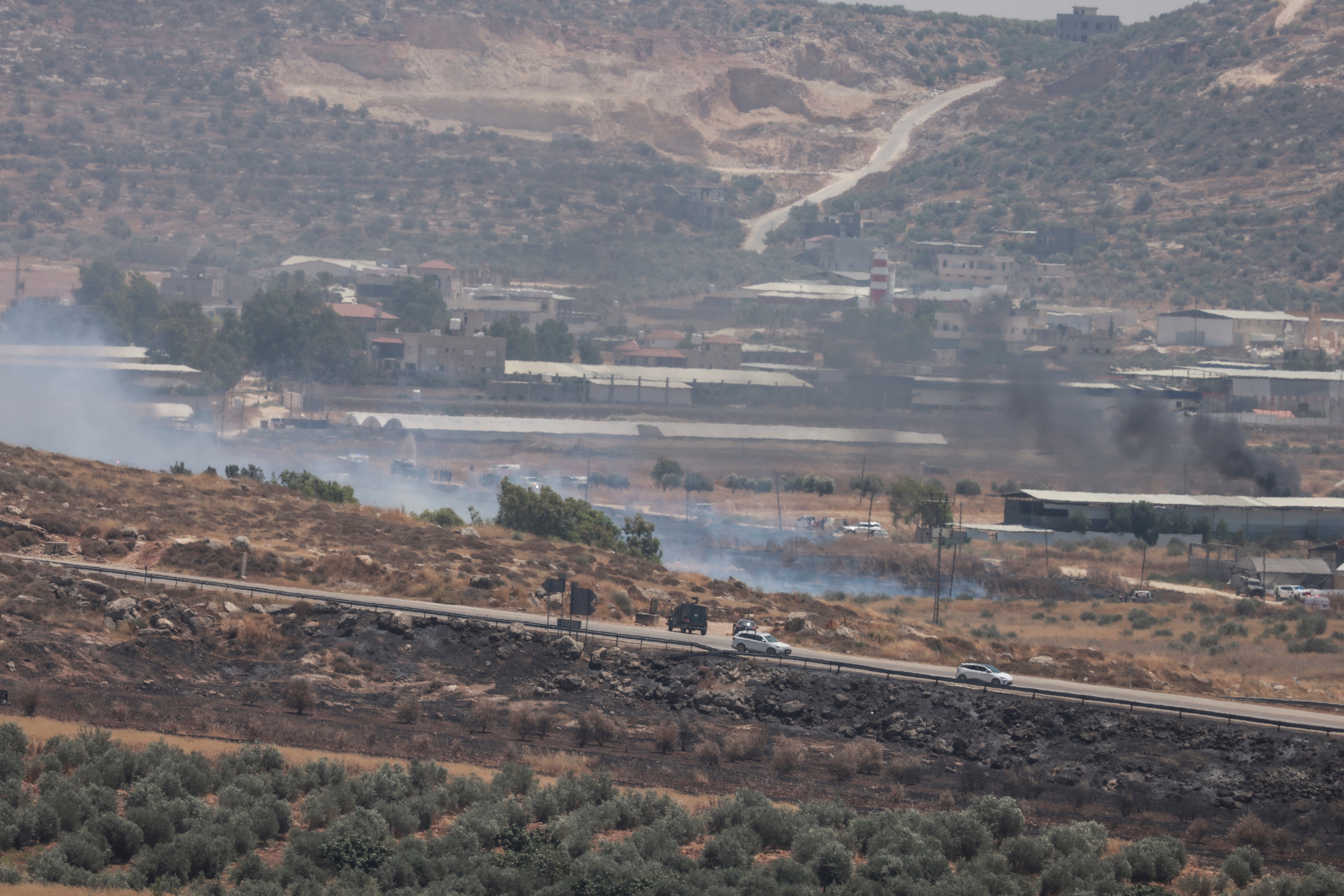 Vehicles belonging to Israeli settlers are parked along the main road near Jewish settlement of Elon Moreh, as smokes rises from fires in the Israeli occupied West Bank, close to the Palestinian village of Beit Furiq (background) on July 23, 2026. (