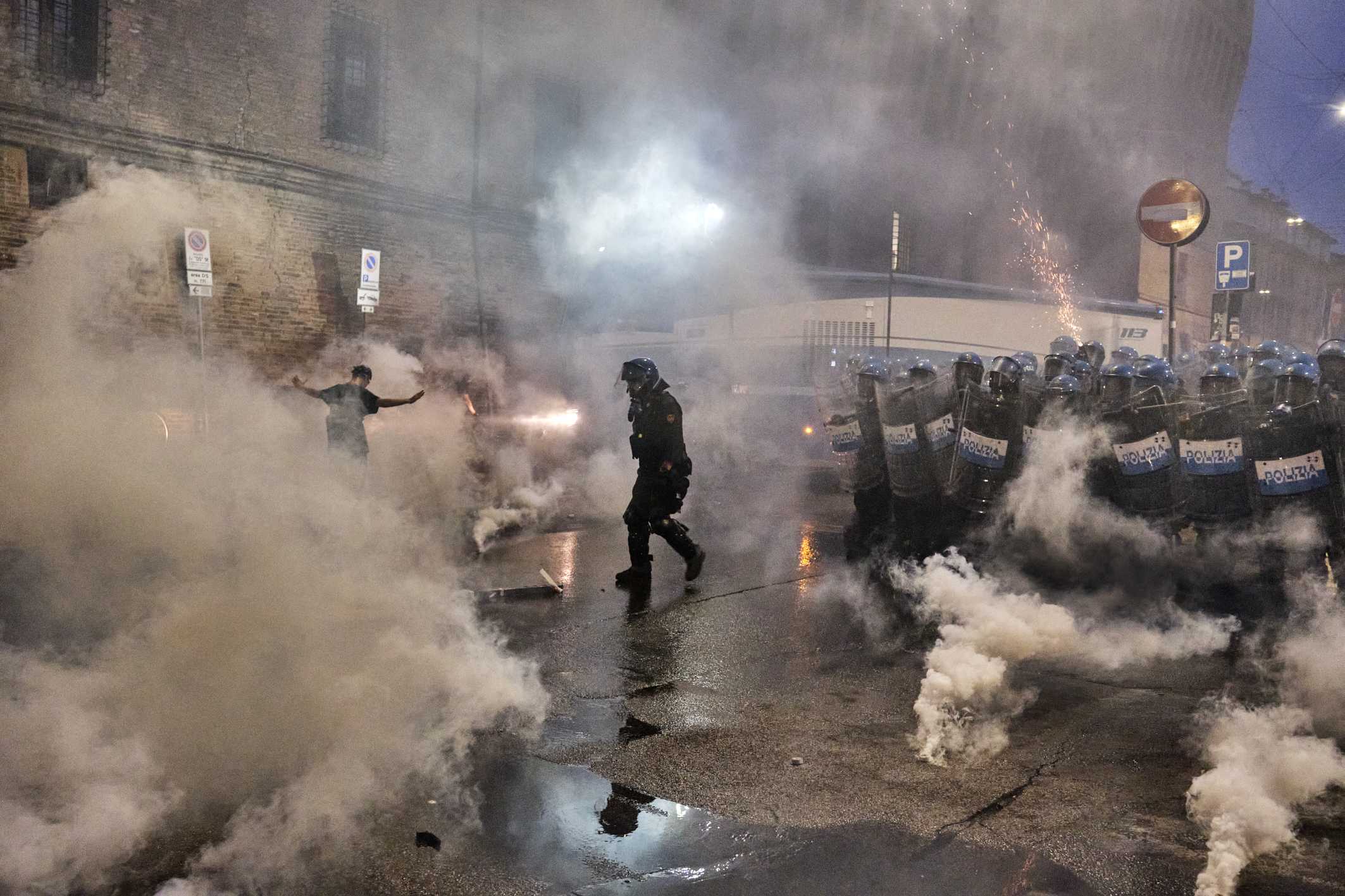 A protester moves through smoke as police stand nearby during clashes in Bologna following demonstrations over Abderrahim Fakir’s death.