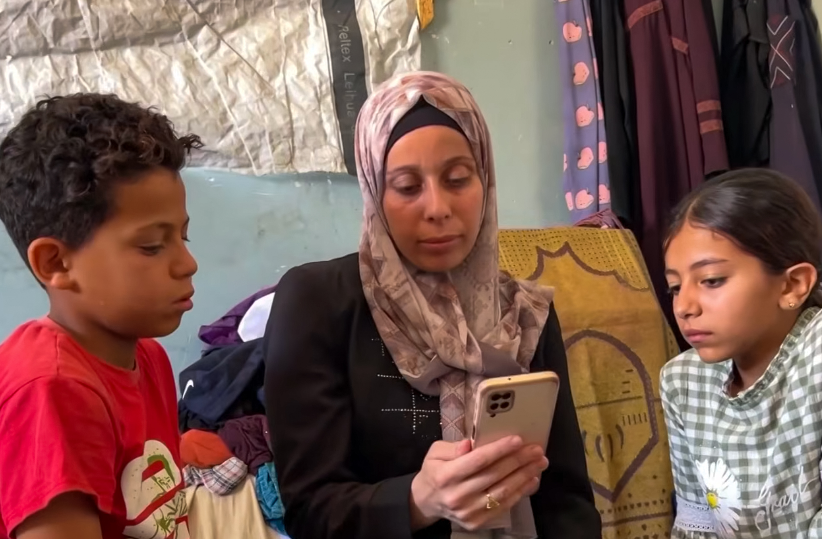 The wife and children of missing Palestinian Nafez Abed look at a phone screen in Gaza. The family remains trapped in agonizing uncertainty, not knowing if he was killed or is being held in Israeli detention. [Screengrab\Al Jazeera]