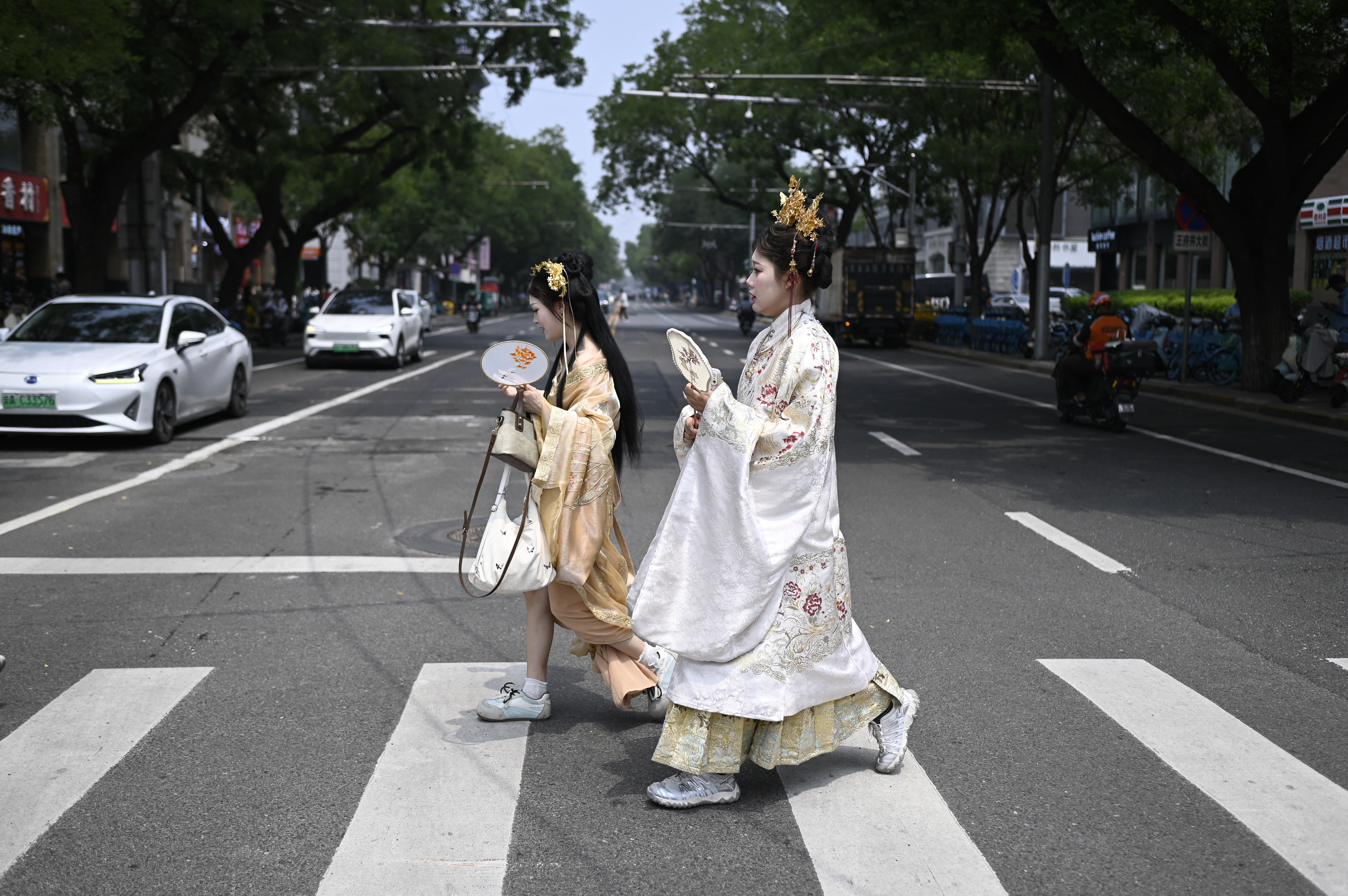 Two women wearing traditional clothes cross a street on a hot day in Beijing on July 2, 2026. (Photo by WANG Zhao / AFP)