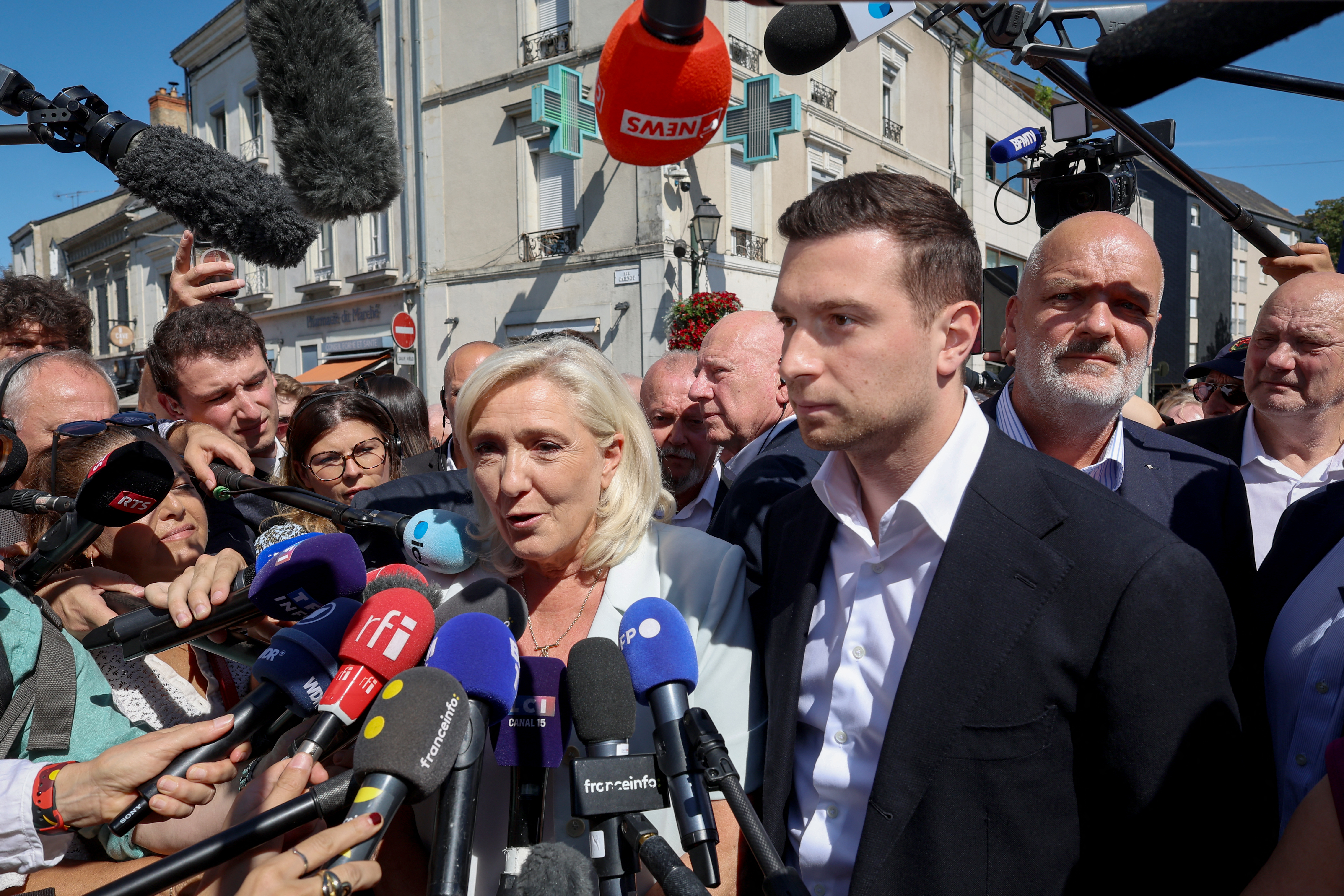 French far-right party Rassemblement National (RN) party leader Marine Le Pen (C) is surrounded by journalists as she arrives with RN president Jordan Bardella (3rd R) and the party's bodyguard Thierry Legier (2nd R) for a campaign gathering in the western central France city of La Fleche on July 8, 2026, a day after she announced her candidacy for the 2027 French presidential election despite an appeals court confirmed her embezzlement conviction.