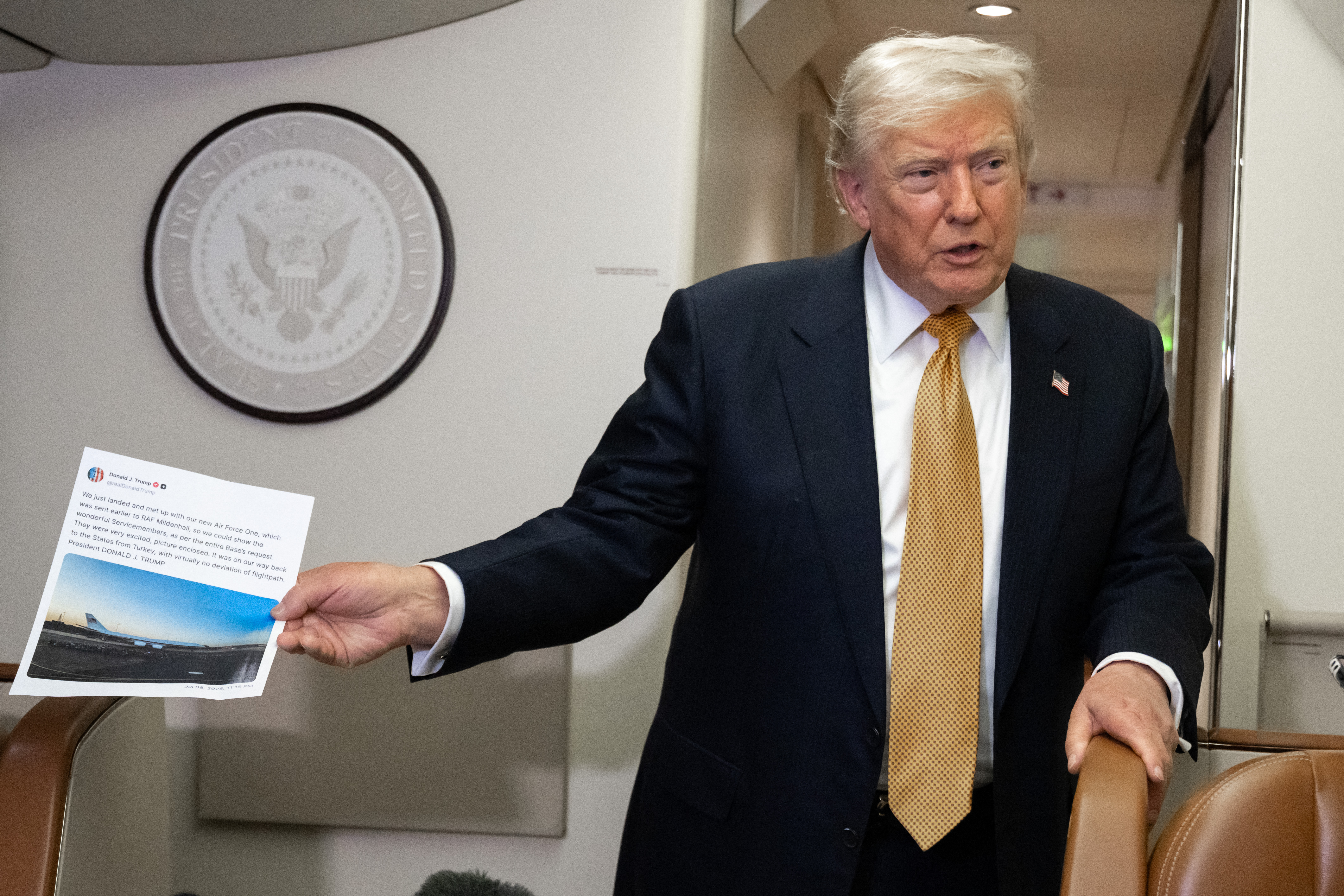 US President Donald Trump holds up a copy of his Truth Social post about Air Force One as he speaks with the media aboard Air Force One shortly after departure from Mildenhall Air Force Base in the United Kingdom, after he switched from the old VC-25A Air Force One to the newer VC-25B Bridge Air Force One, enroute to Washington, on July 8, 2026.