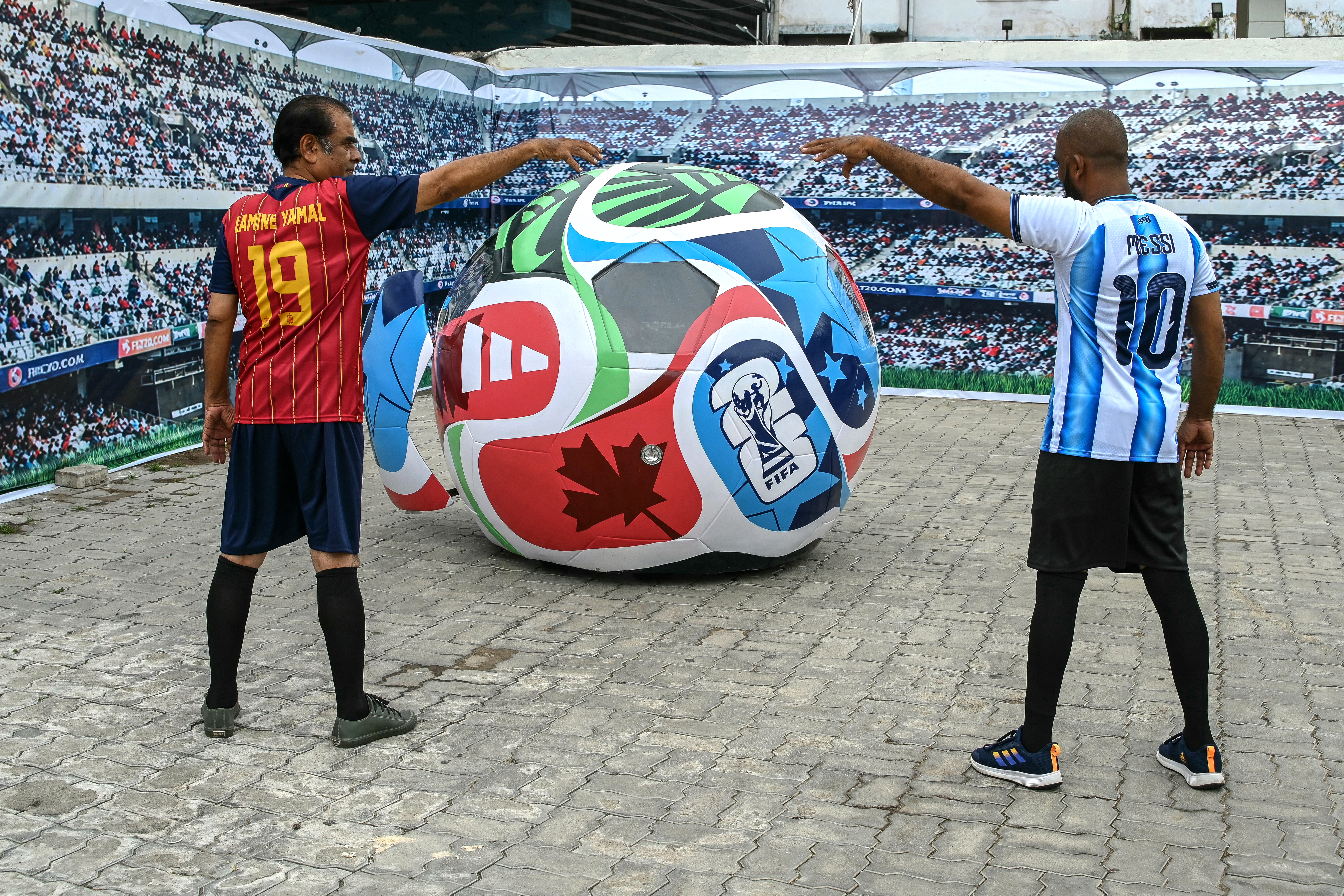 Fans wearing jerseys of Spanish footballer Lamine Yamal (L) and Argentinian footballer Lionel Messi pose with 2026 FIFA World Cup official ball-themed car at a museum in Hyderabad on July 18, 2026 on the eve of the World Cup football tournament final match between Spain and Argentina. (Photo by Noah SEELAM / AFP)