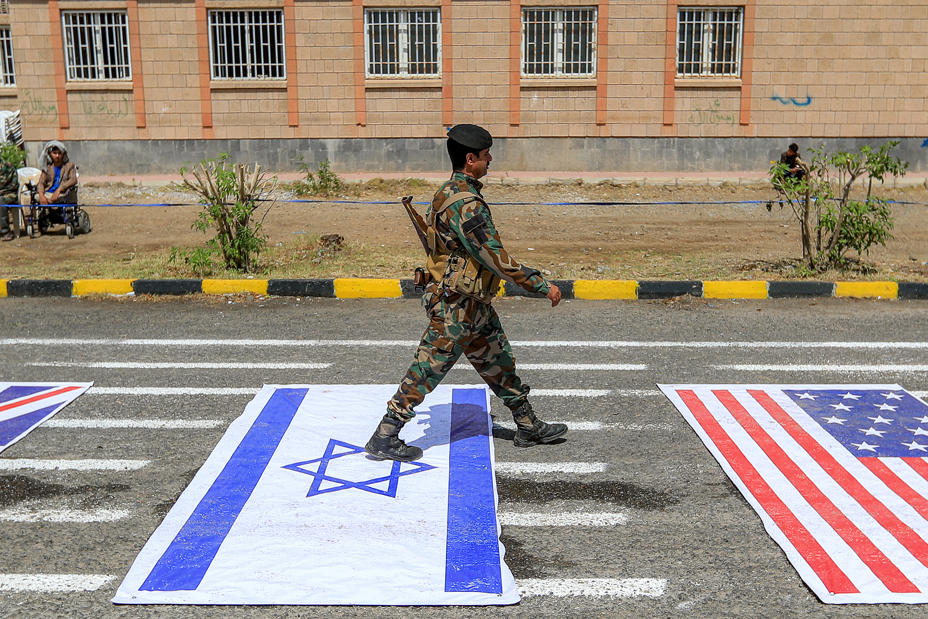 A fighter loyal to Yemen's Houthi movement walks over depictions of the Israeli and US during a demonstration by university students to show their support for the Houthis amid escalating tensions with Saudi Arabia, at the Sanaa University campus in the Houthi-held capital Sanaa on July 22, 2026.