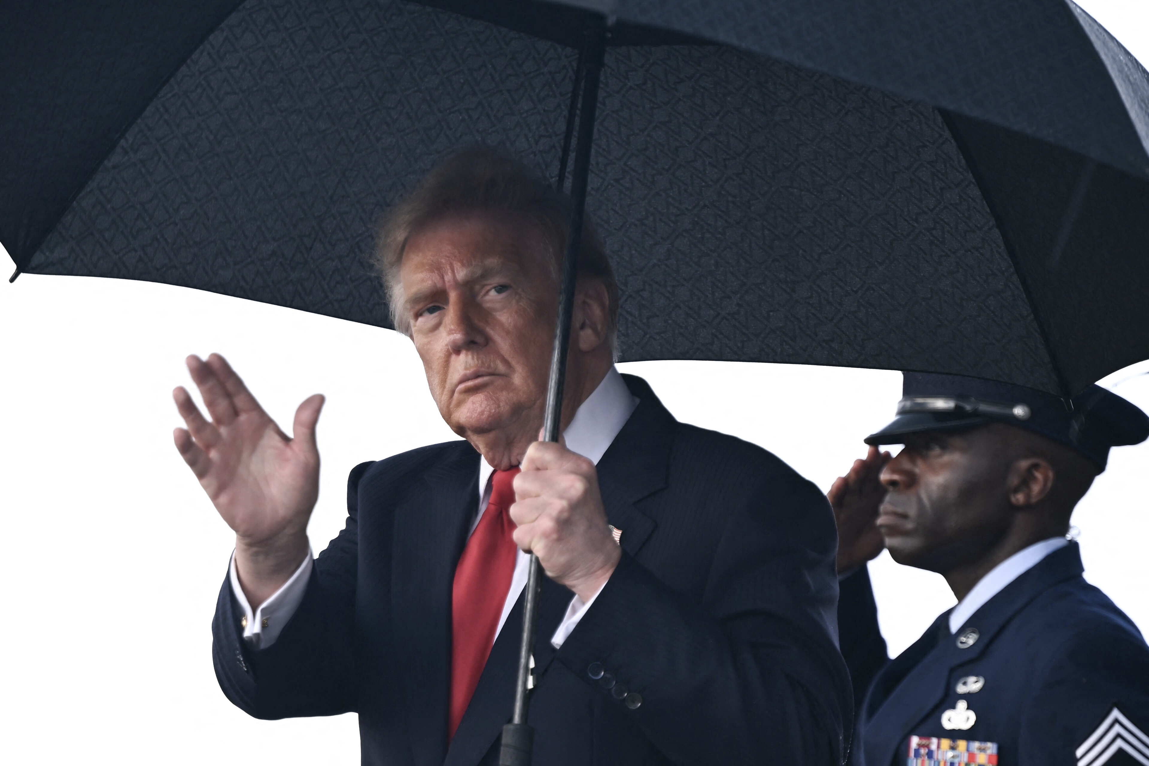 A man in a suit next to a uniformed officer under an umbrella