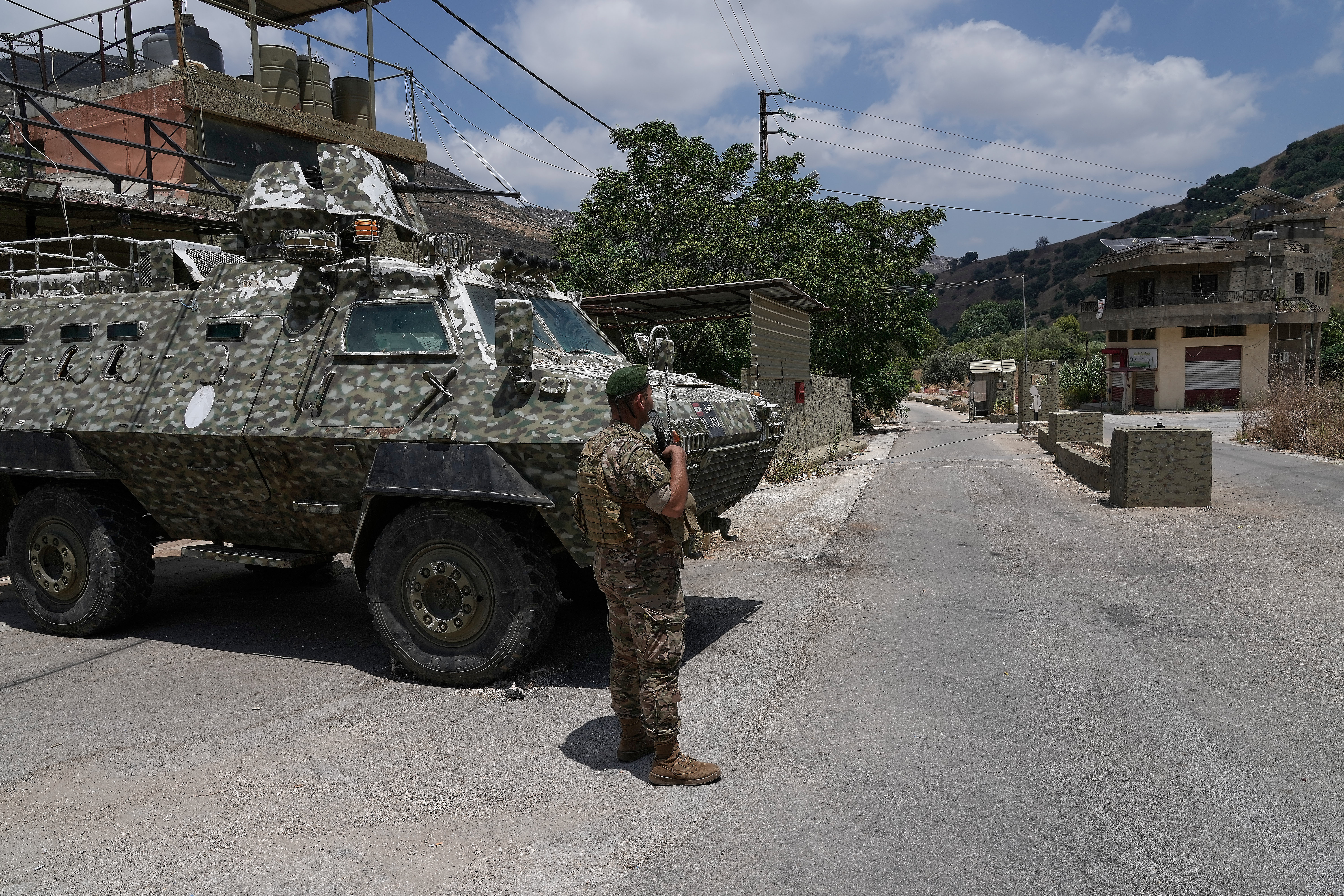 A soldier stands near a military vehicle in a village