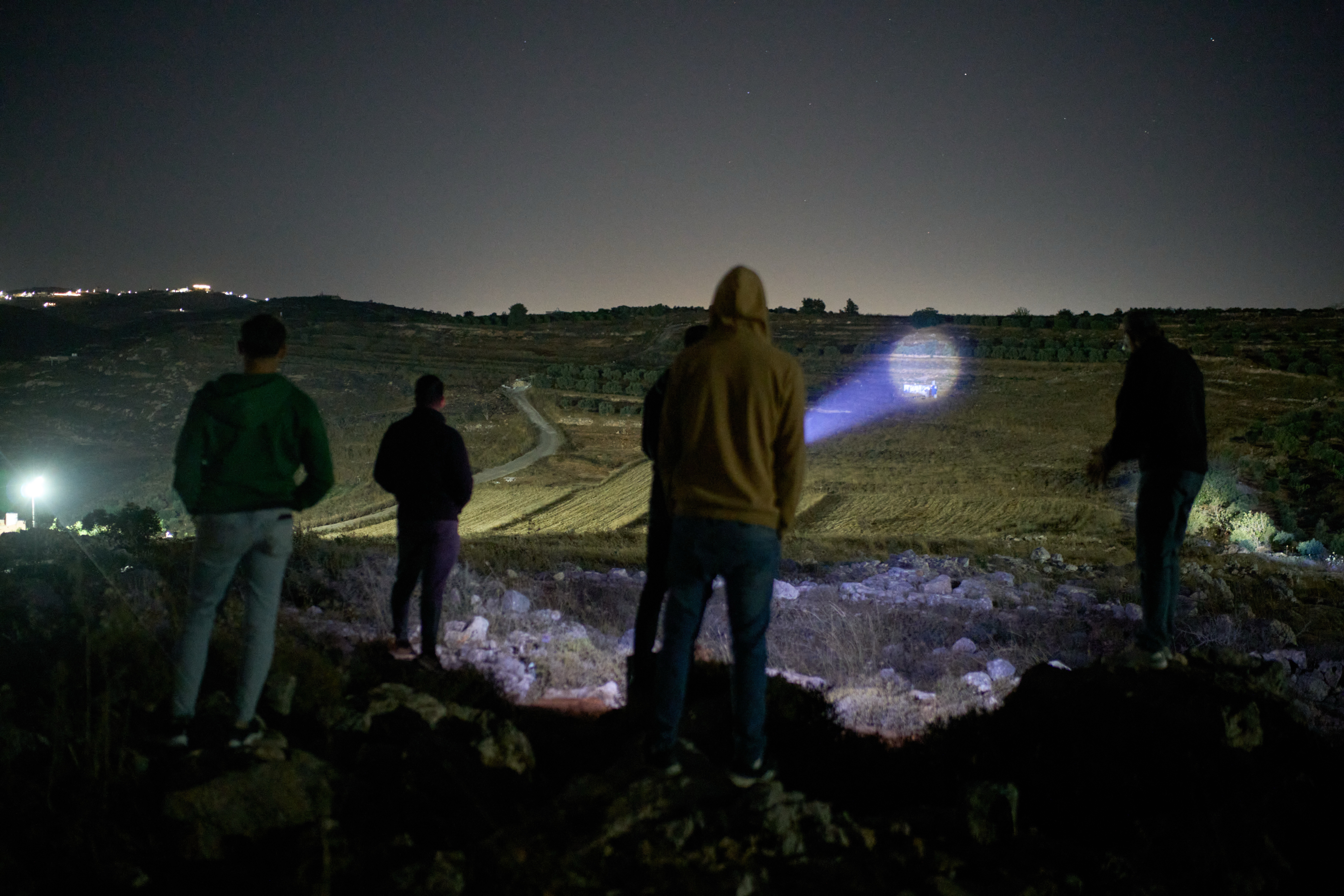 A Palestinian uses a flashlight after spotting Israeli settlers on a nearby hill while taking part in a night watch with other volunteers to guard against settler attacks on the West Bank village of Sinjil, Thursday, July 16, 2026. [AP]