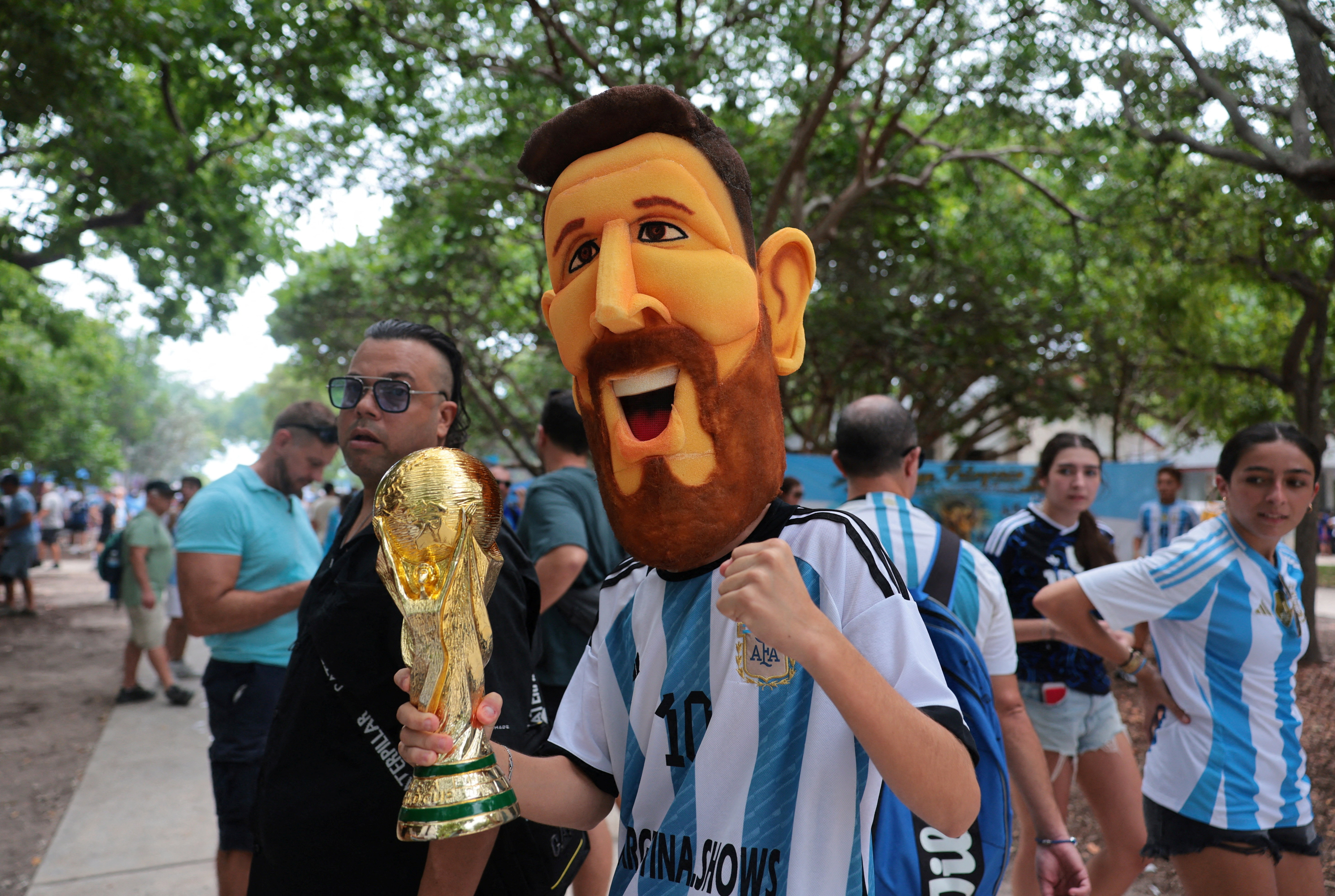 Argentina fan wears a Lionel Messi head and holds a replica World Cup trophy in a parade.