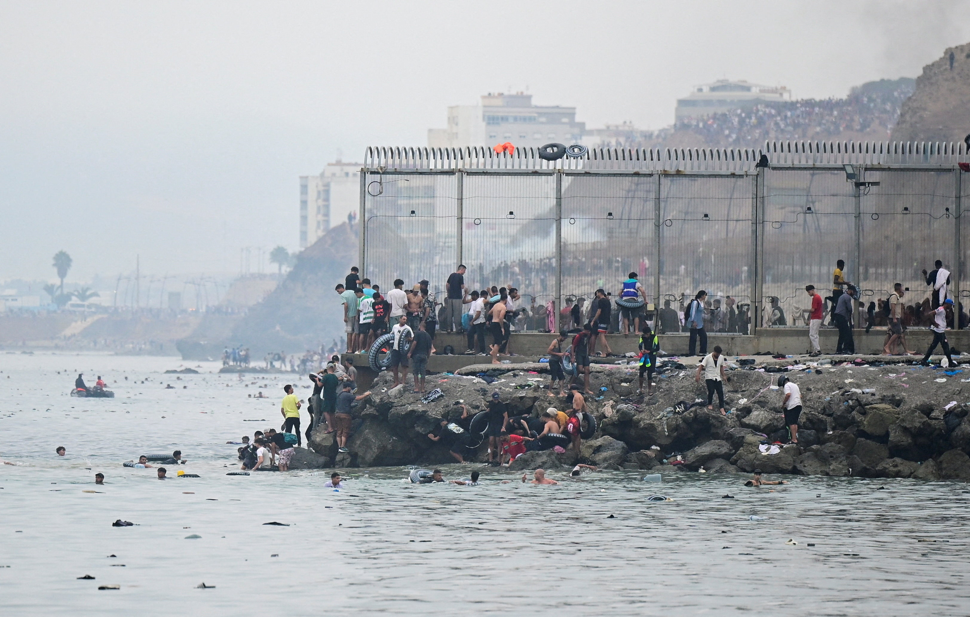 People gather by a border fence at a beach.