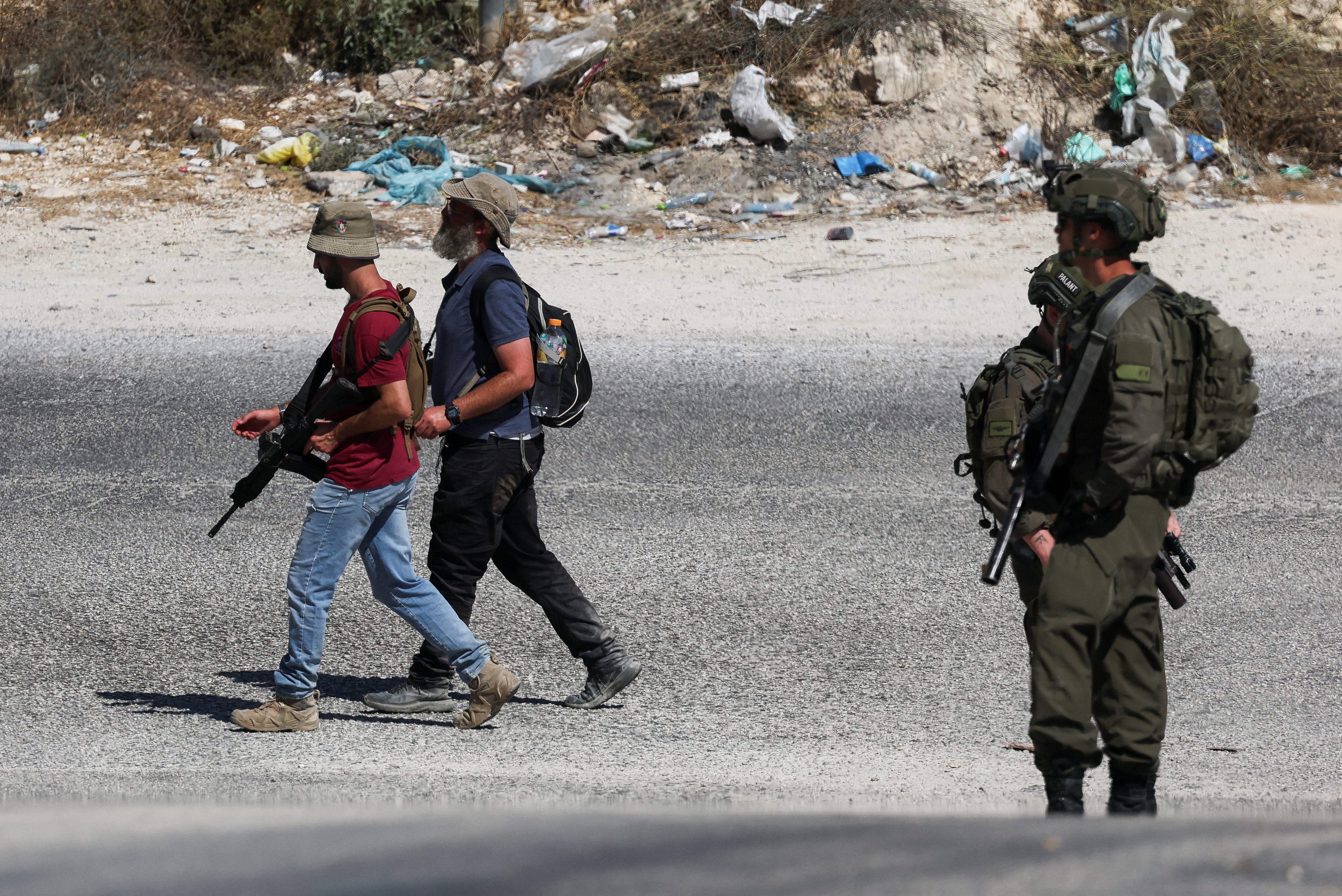 Israeli settlers walk in the Palestinian village of Tal, as an Israeli soldier stands guard, in the Israeli-occupied West Bank, July 31, 2026. REUTERS/Ammar Awad