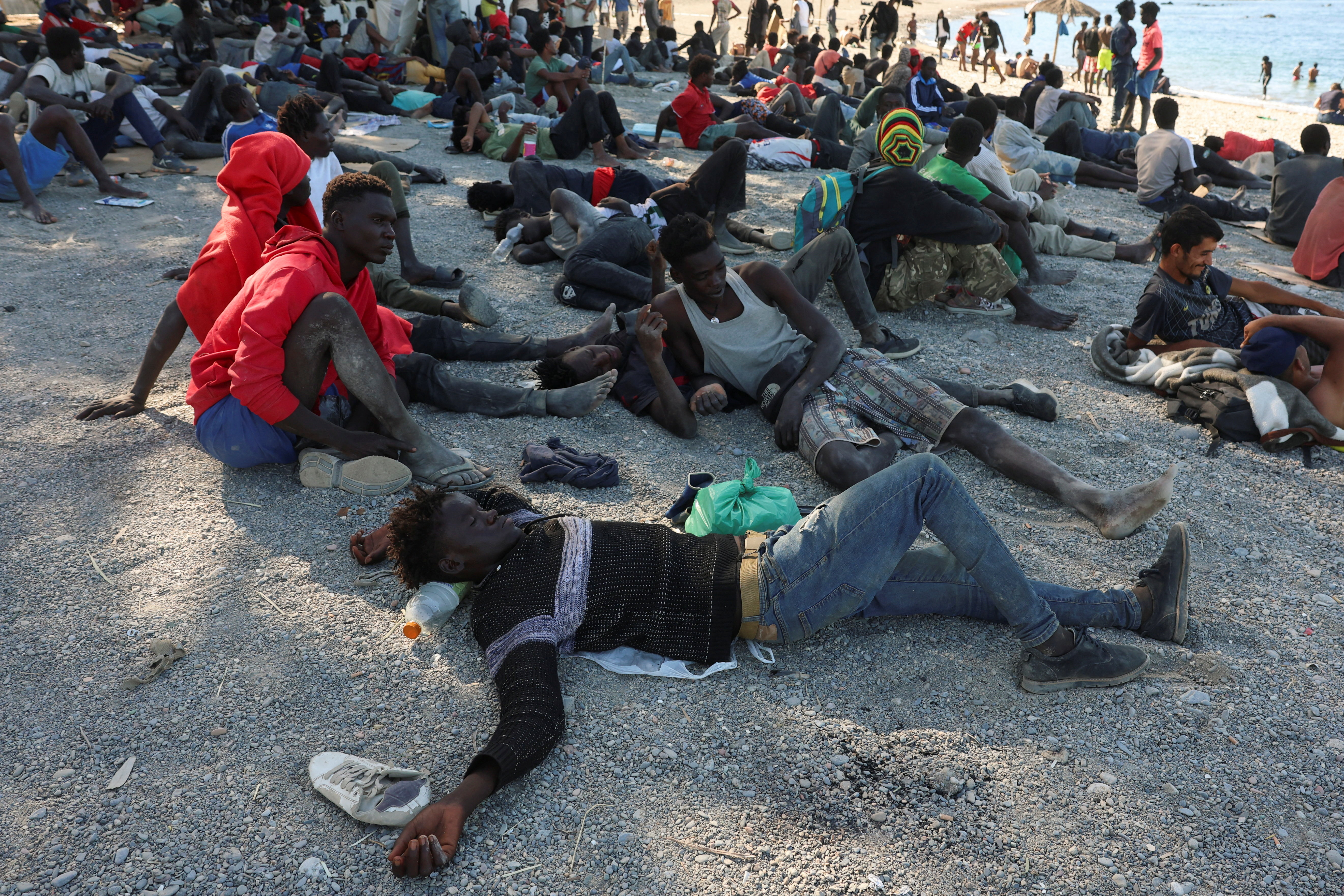 People sit and lie on a beach in their clothes.