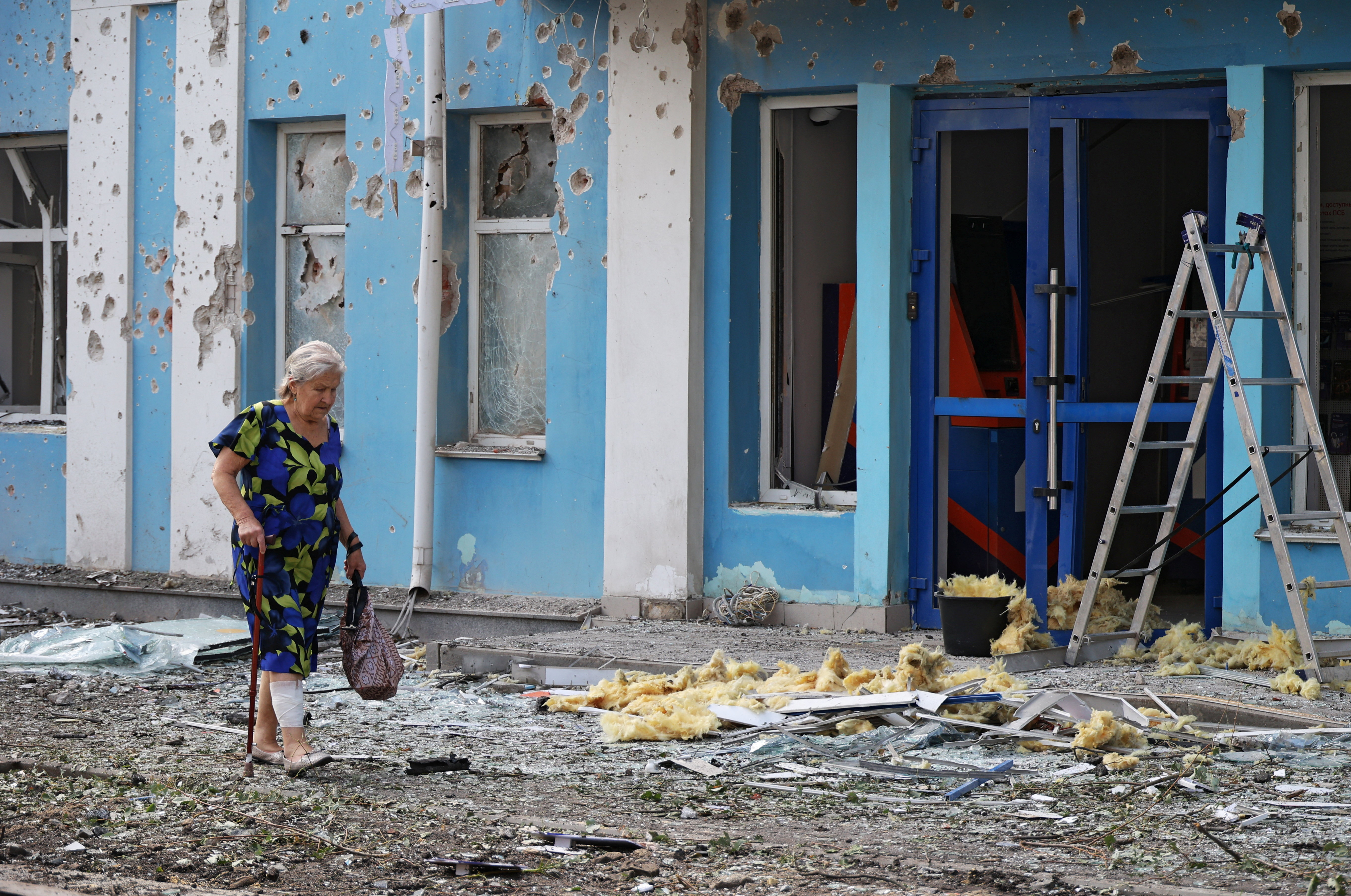 A woman walks past a bank damaged during an overnight Ukrainian drone attack in Belgorod, Russia on August 9, 2026.