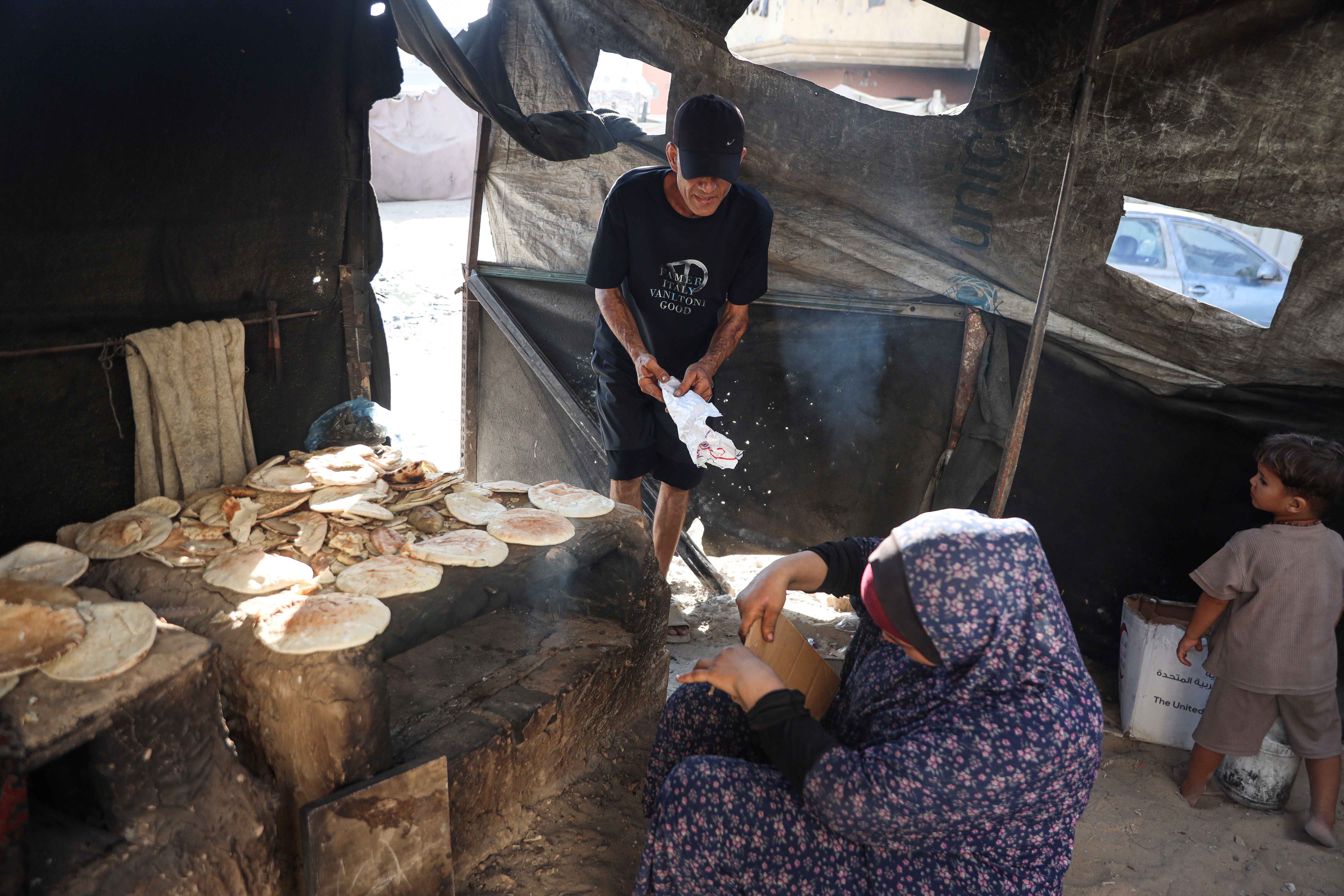 Hasnaa Mansour, 43, sits beside the clay oven she uses to bake food for sale, but struggles to light it because of the shortage of lighters [Abdelhakim Abu Riash/ Al Jazeera]