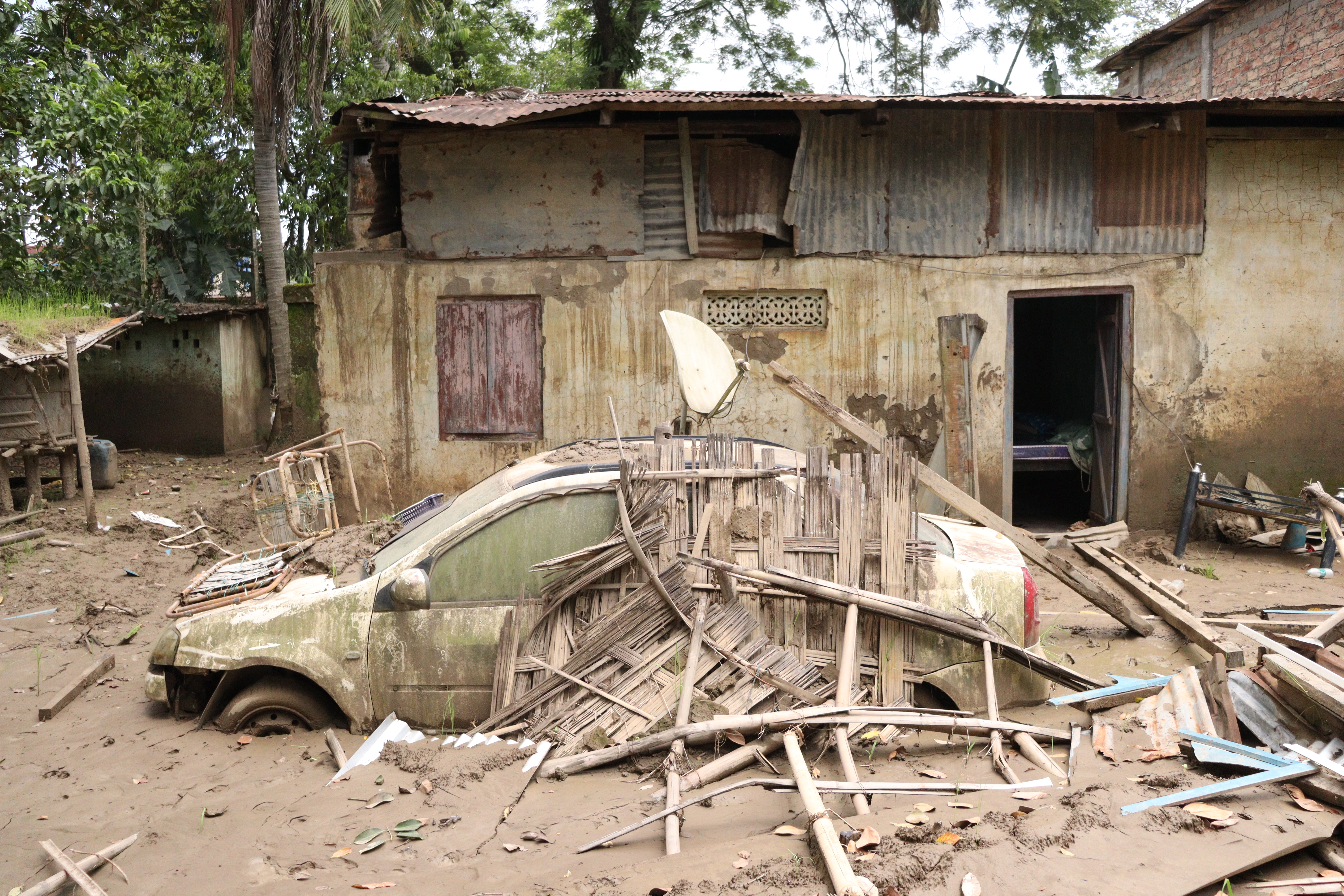 A car buried in silt in front of a home affected by floodwater in Sivasagar in India's Assam [Arshad Ahmed/Al Jazeera]