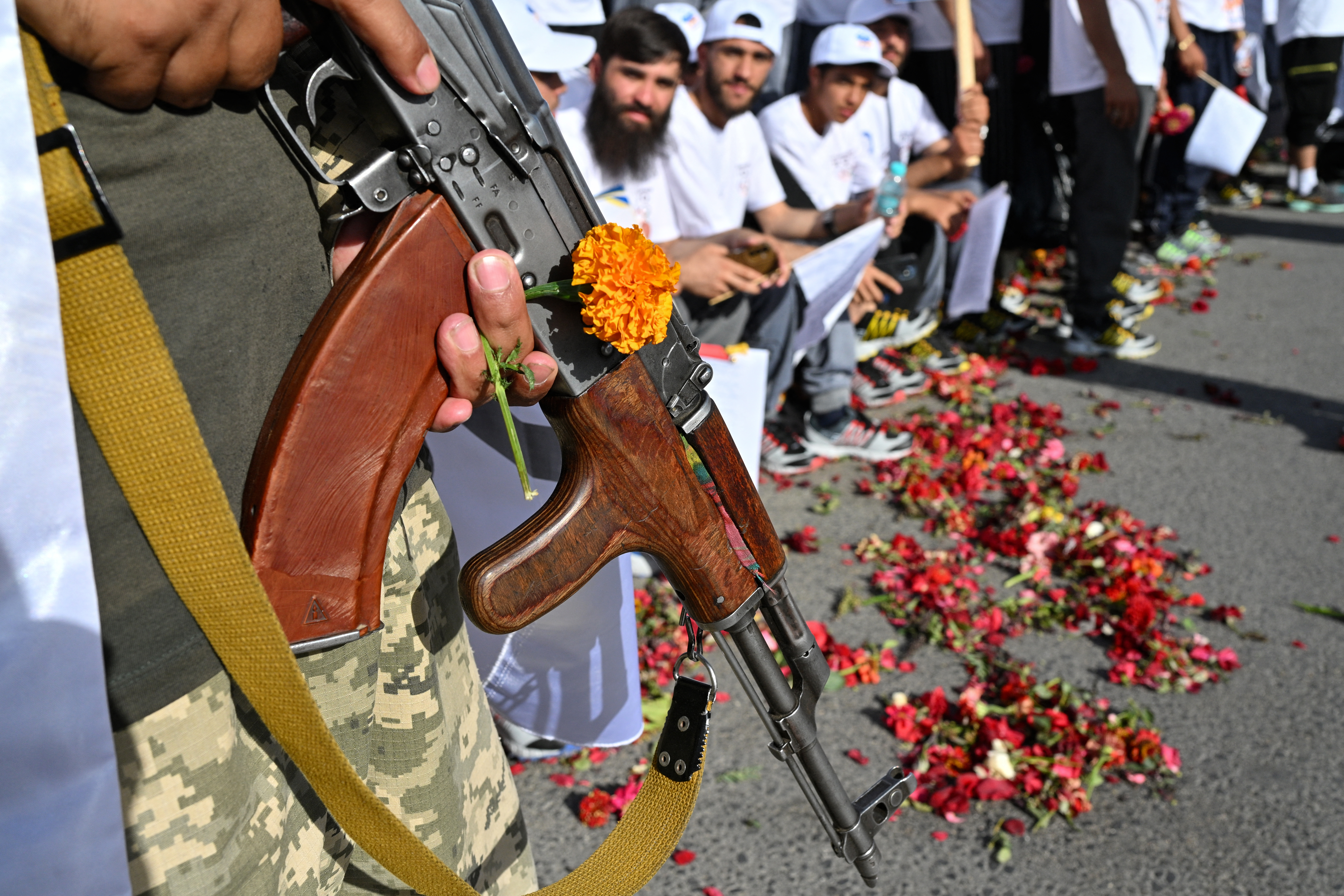 A Taliban security personnel holds a marigold flower and a gun.