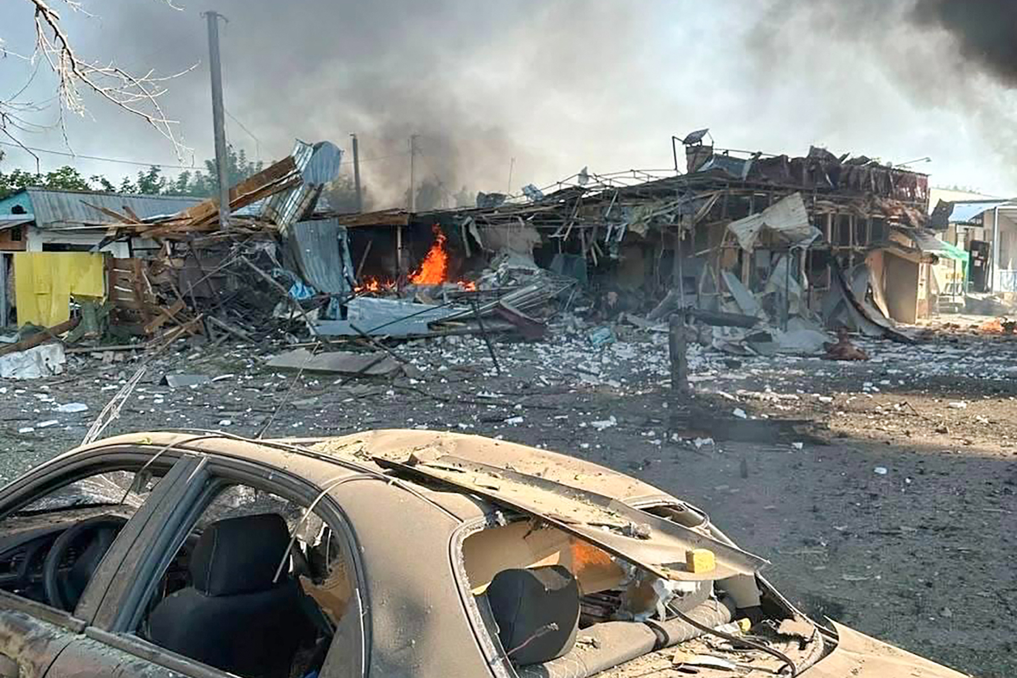 A destroyed car next to a burning building.